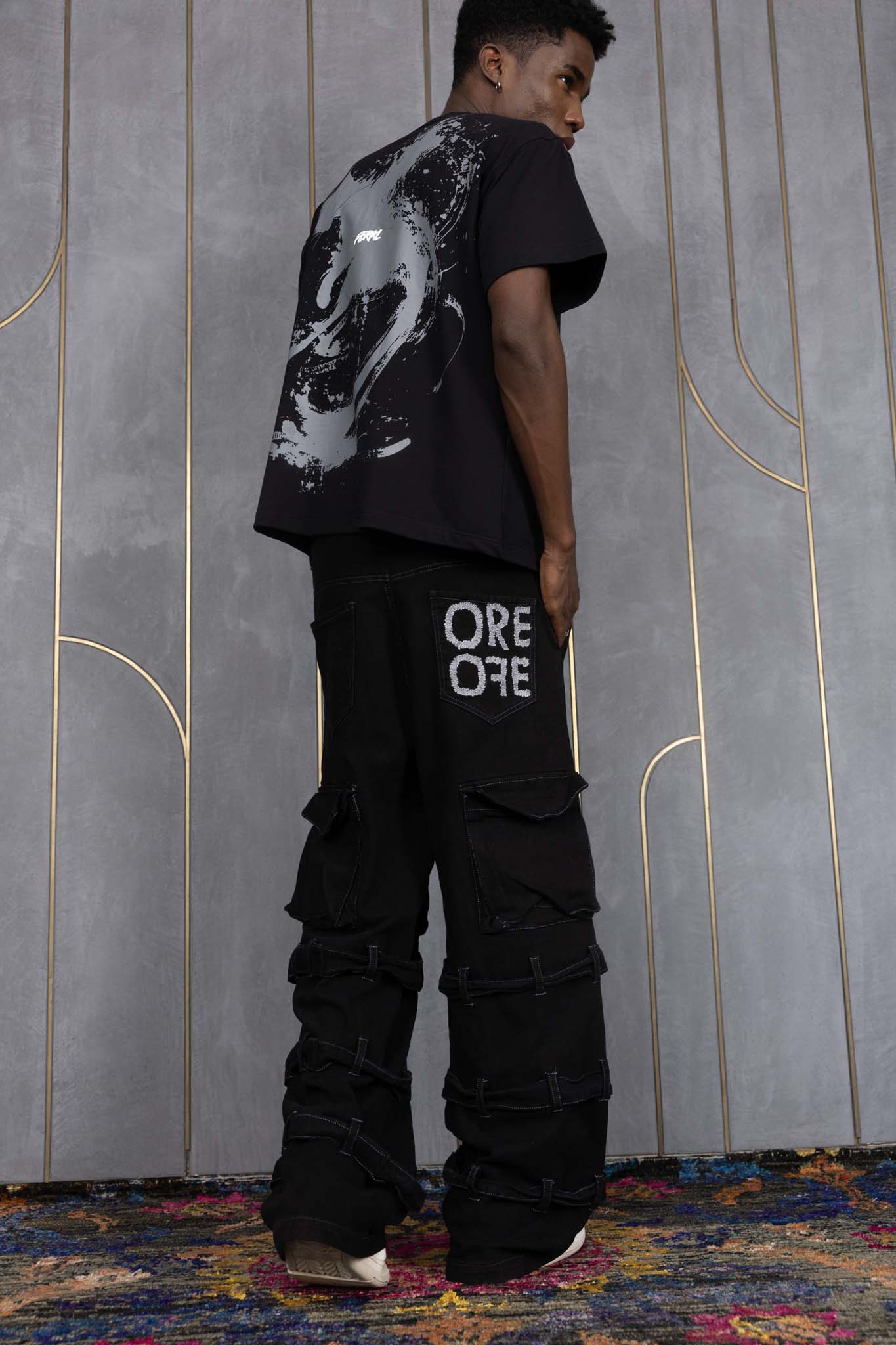 Person wearing ORE OFE's blackout t-shirt & denim and standing in front of a grey wall on a textured rug