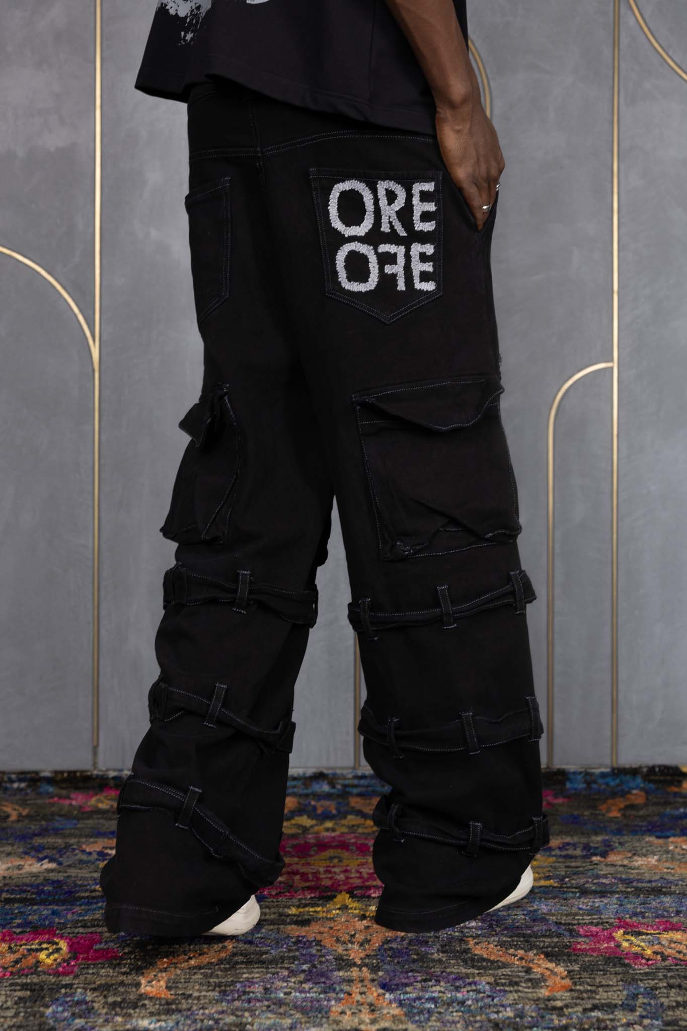 Person wearing ORE OFE's blackout t-shirt & denim and standing in front of a grey wall on a textured rug