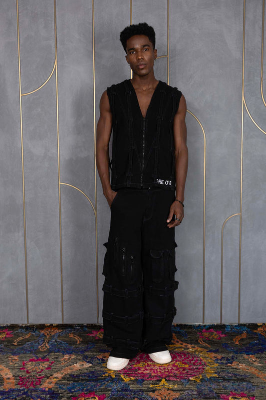 Person wearing ORE OFE's blackout vest & denim and standing in front of a grey wall on a textured rug