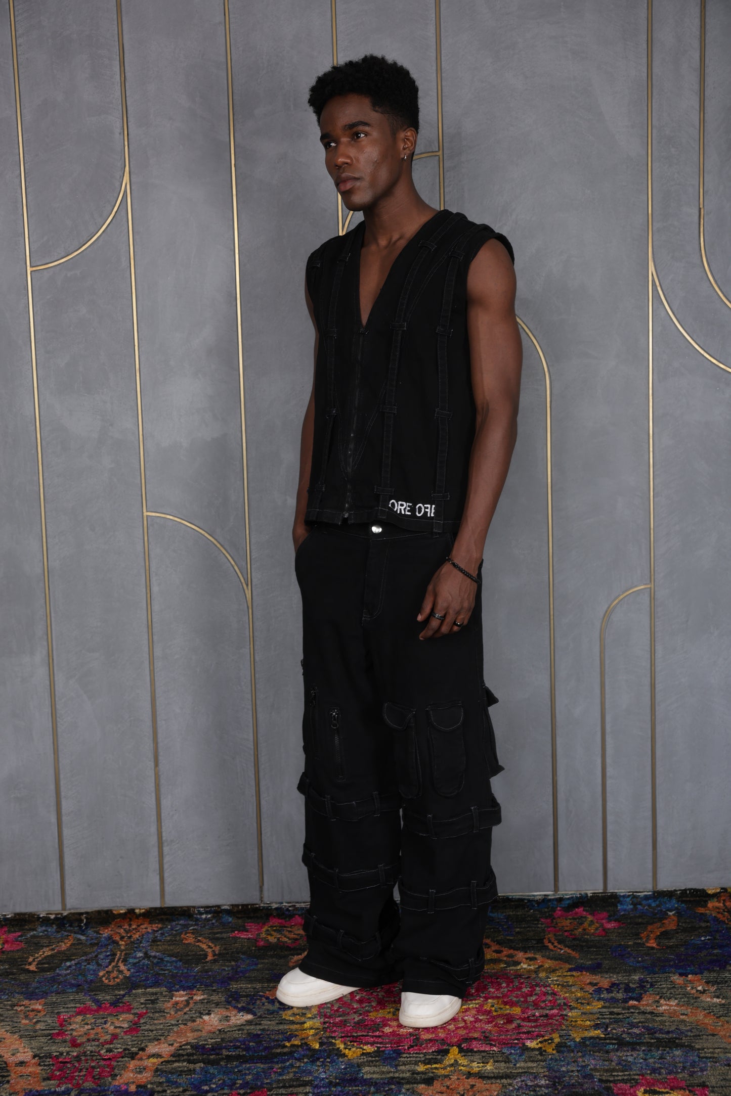 Person wearing ORE OFE's blackout vest & denim and standing in front of a grey wall on a textured rug