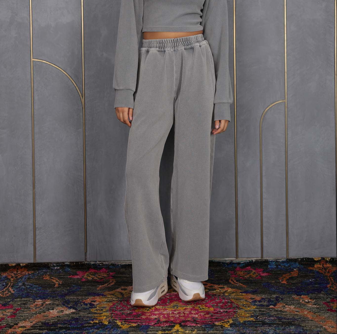Woman wearing ORE OFE's grey waffle tank & bottom standing in front of a grey wall on a textured rug