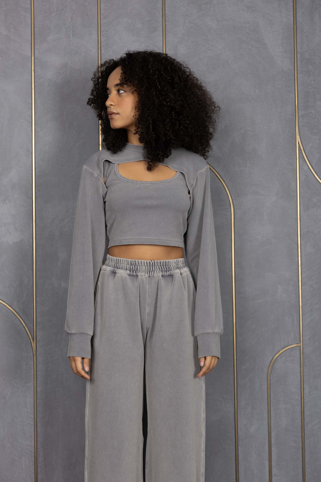 Woman wearing ORE OFE's grey waffle tank & bottom standing in front of a grey wall on a textured rug