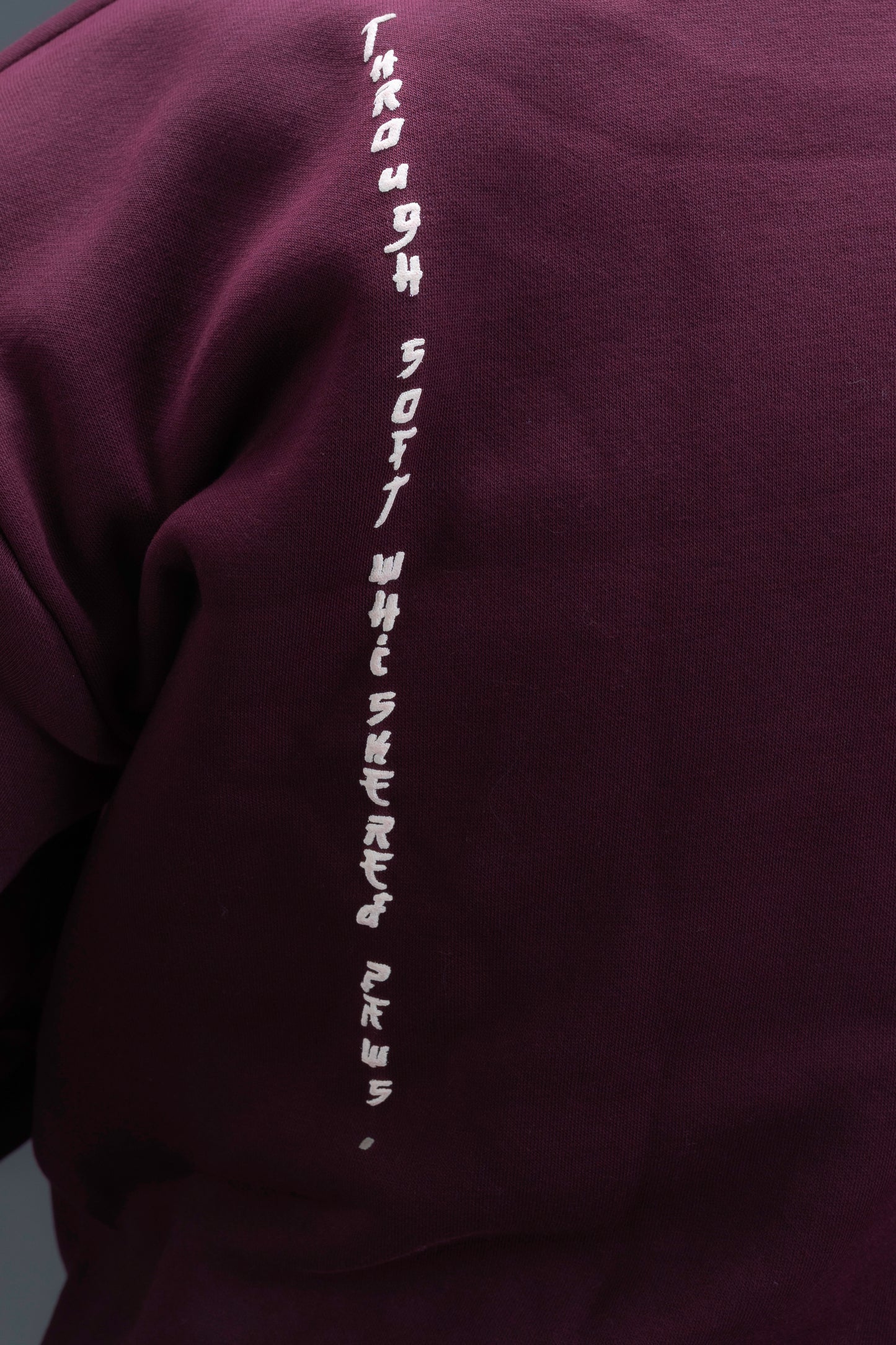 Person wearing a maroon contrast hoodie by ORE OFE with chest & back puff printed design standaing against a dark grey background