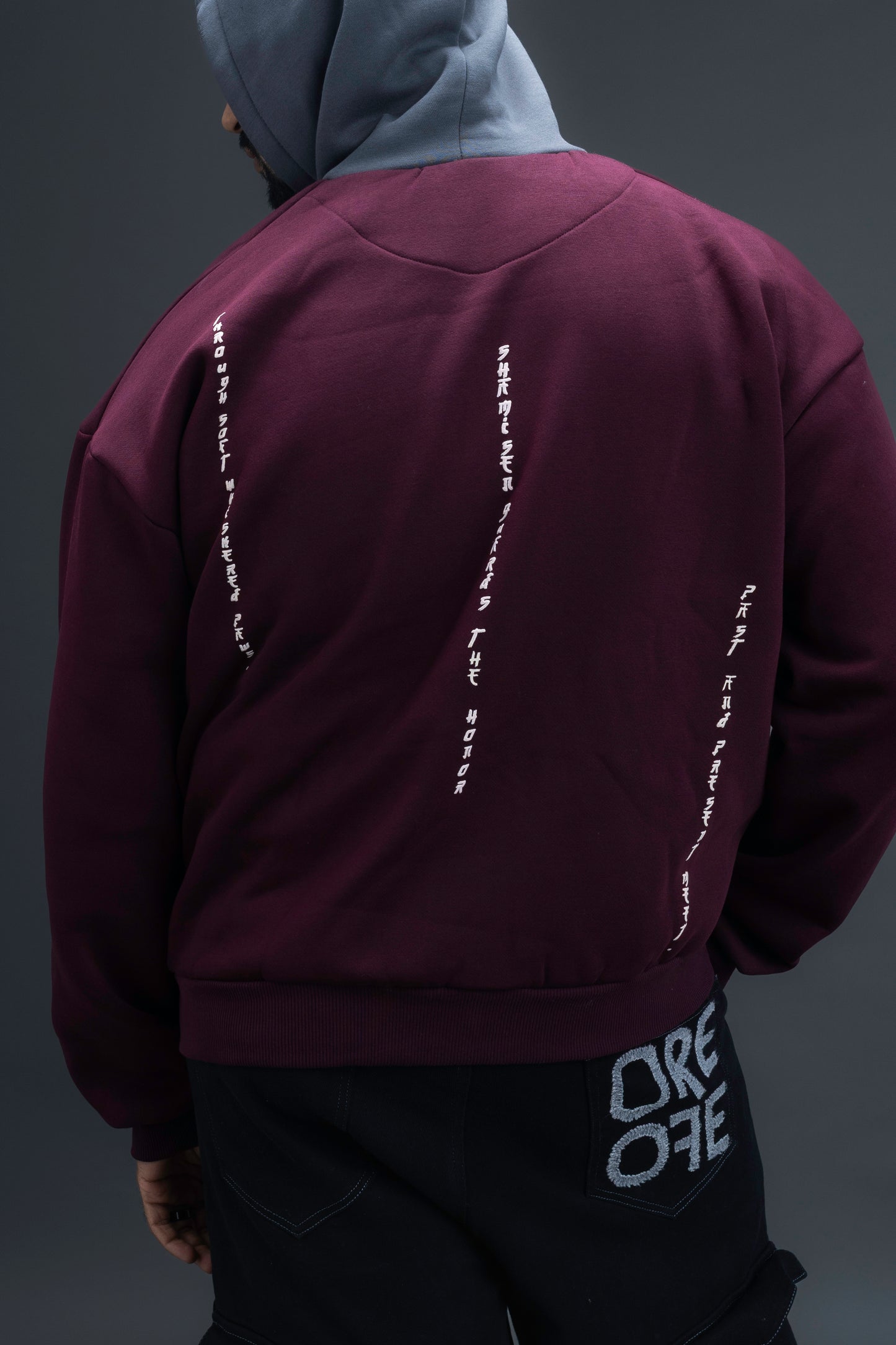 Person wearing a maroon contrast hoodie by ORE OFE with chest & back puff printed design standaing against a dark grey background
