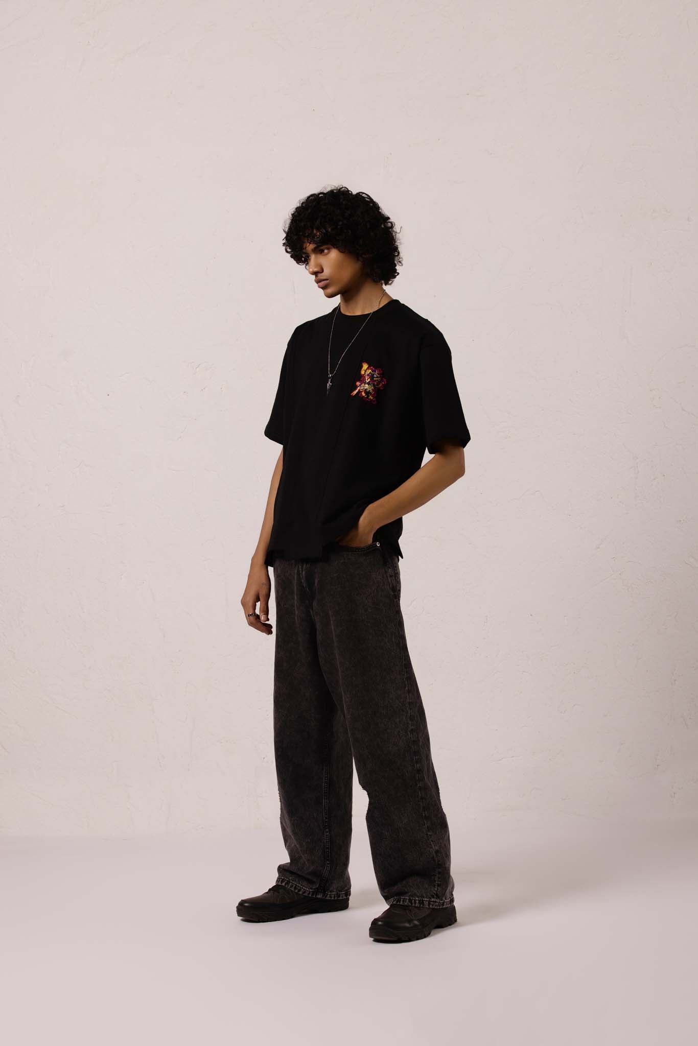 Person wearing a black t-shirt with a small design on a plain background