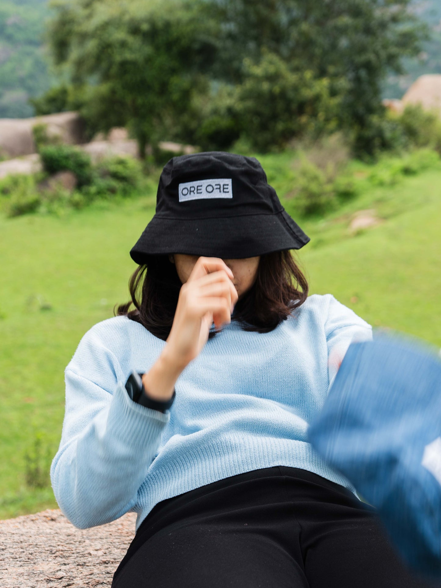 Person wearing a black bucket hat with 'ORE ORE' logo in a natural setting