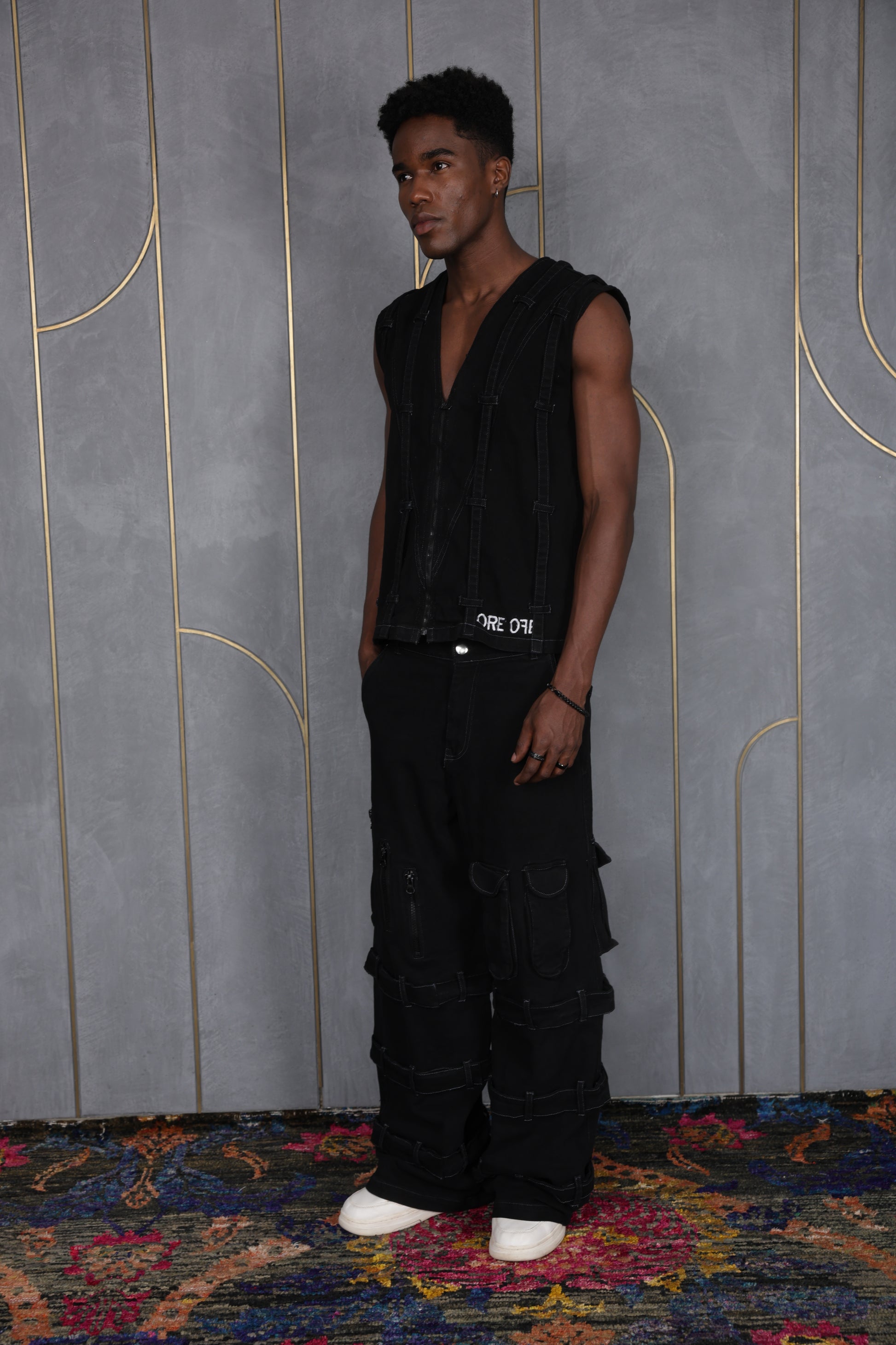 Person wearing ORE OFE's blackout vest & denim and standing in front of a grey wall on a textured rug