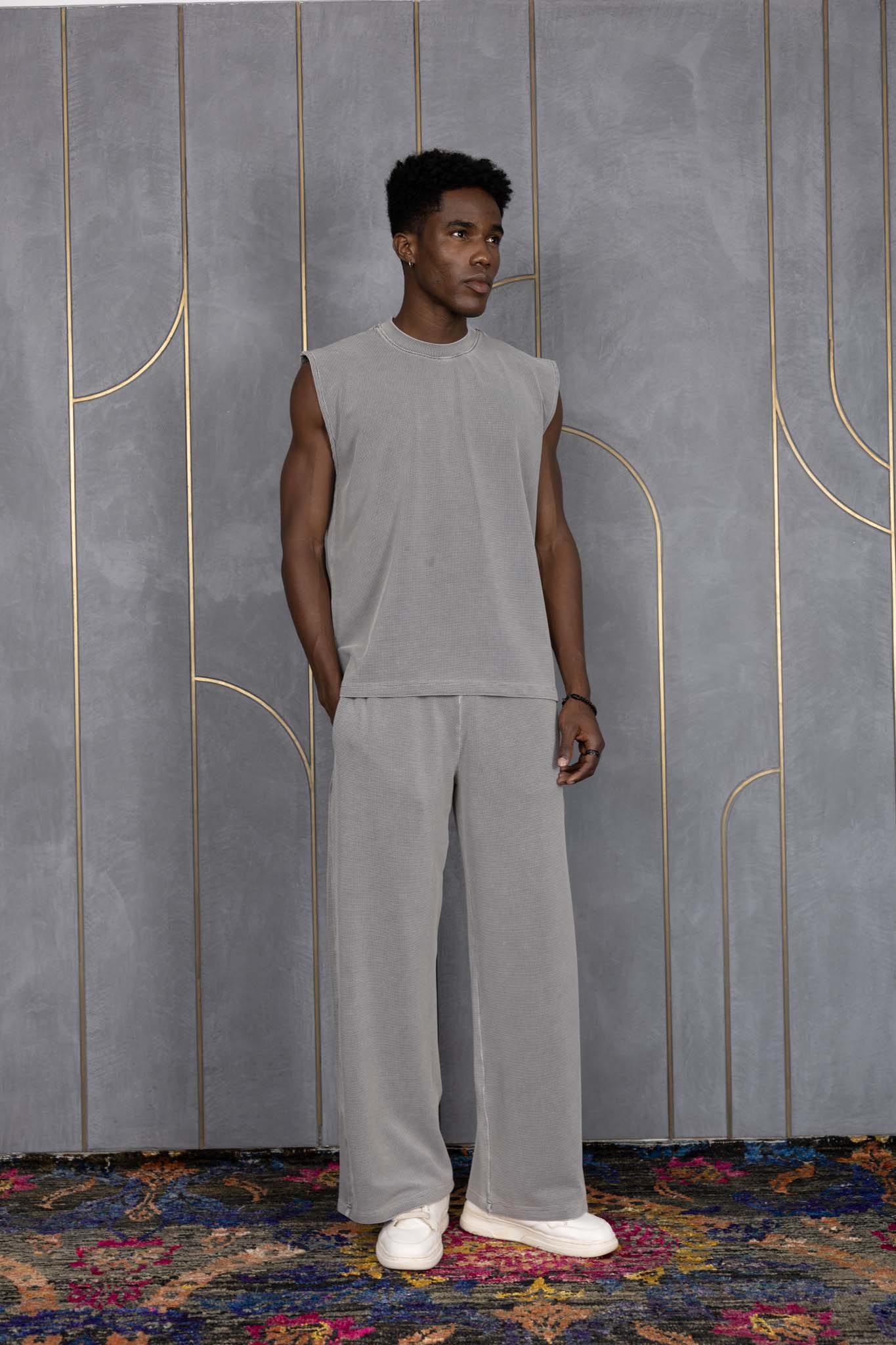 Person wearing ORE OFE's grey waffle tank & bottom standing in front of a grey wall on a textured rug