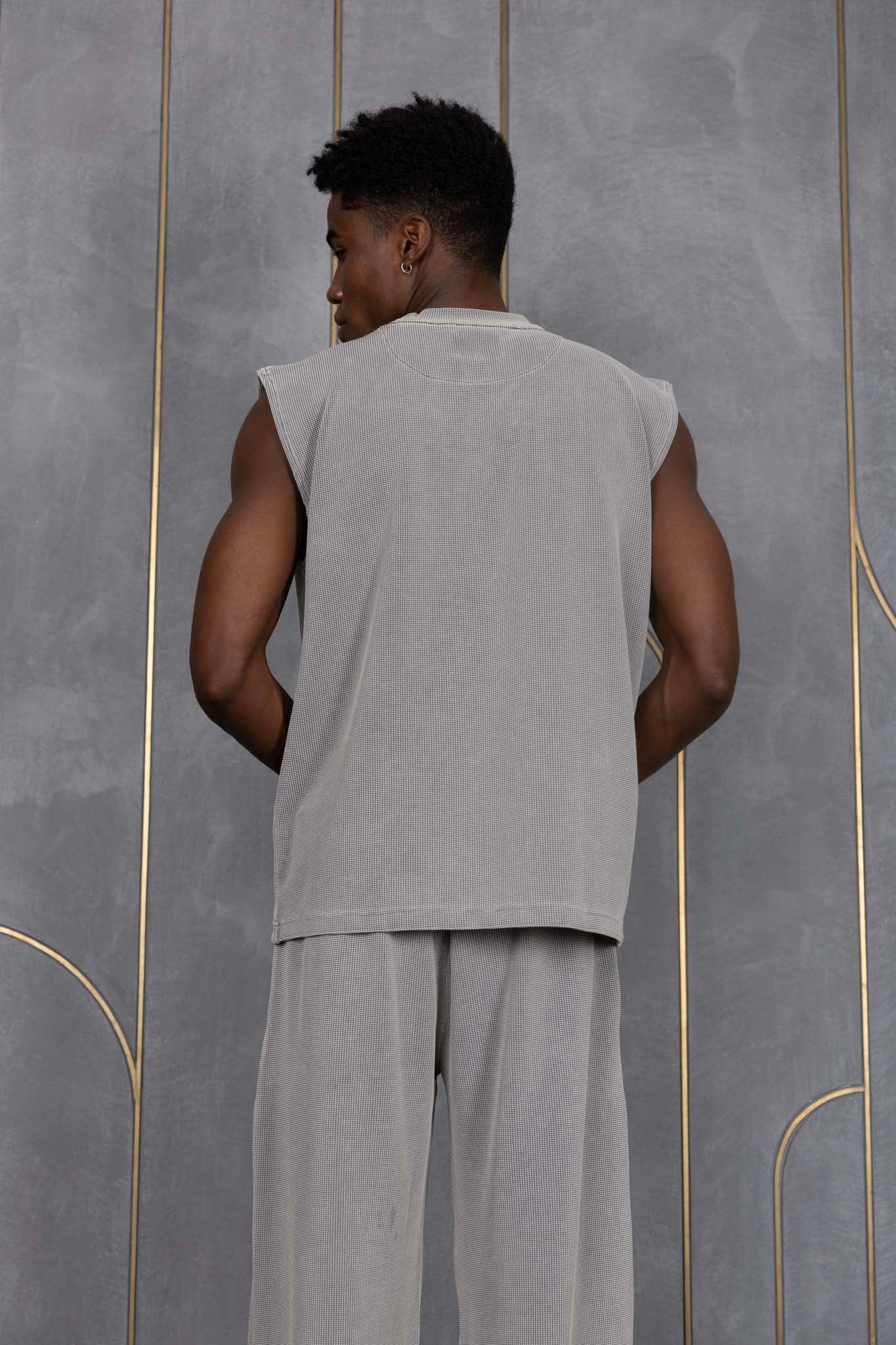 Person wearing ORE OFE's grey waffle tank & bottom standing in front of a grey wall on a textured rug