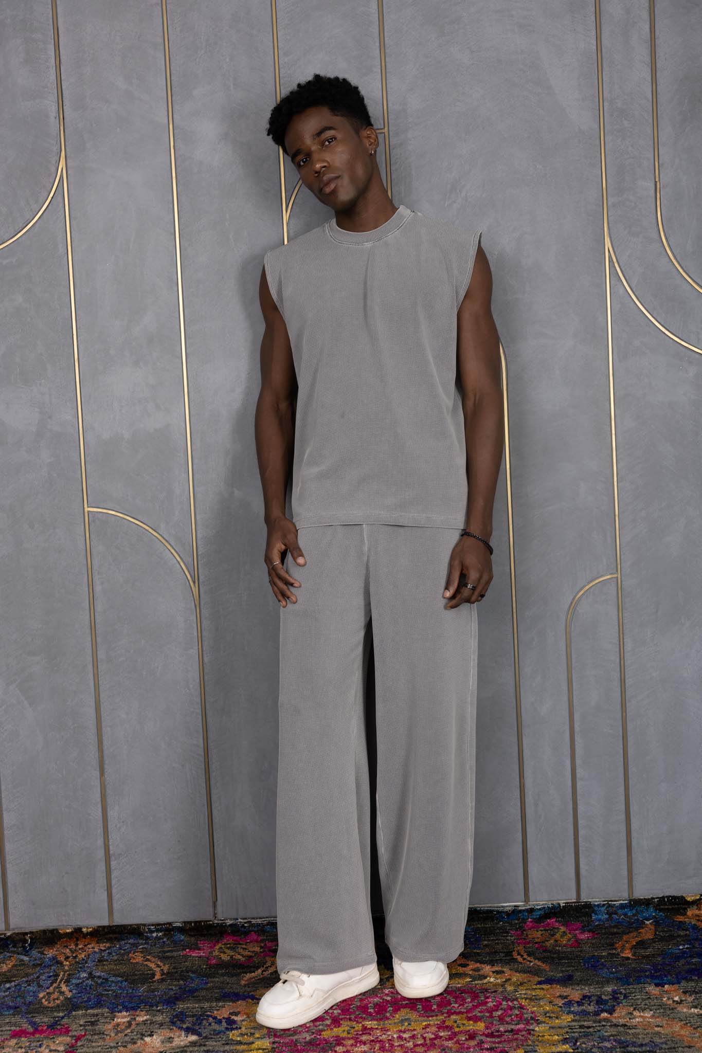 Person wearing ORE OFE's grey waffle tank & bottom standing in front of a grey wall on a textured rug