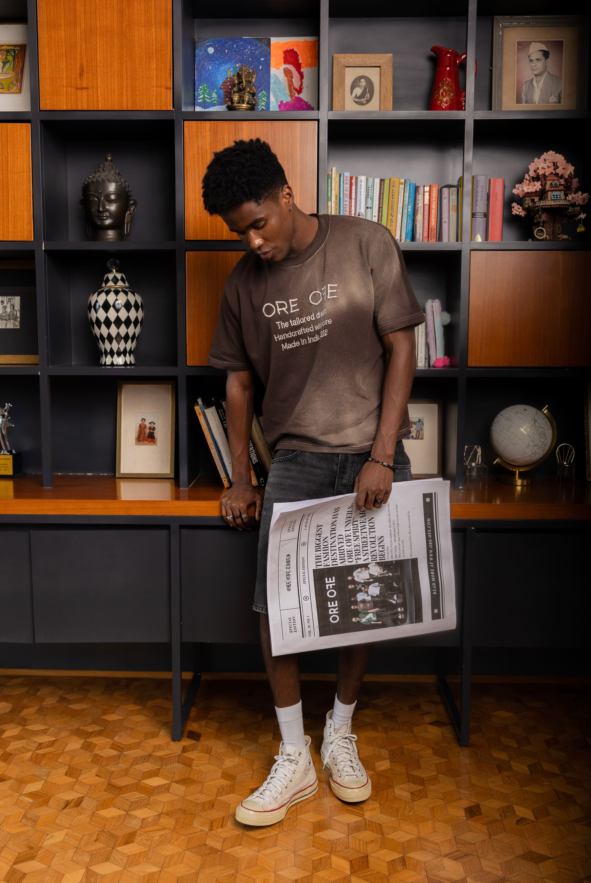 Person holding a newspaper in front of a bookshelf with various items
