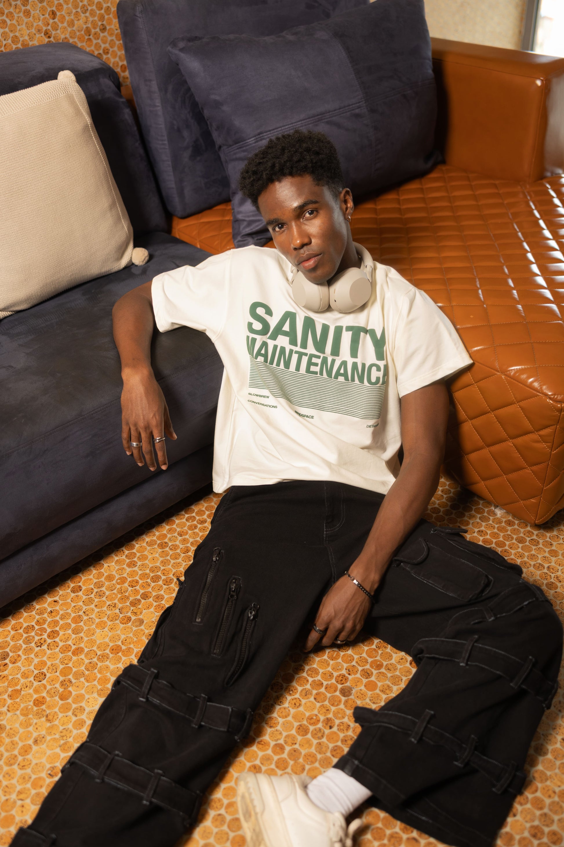 Person wearing a 'SANITY MAINTENANCE' T-shirt and sitting on a patterned floor