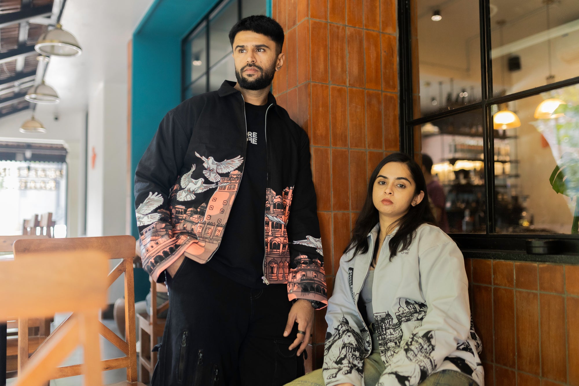 Two people wearing ORE OFE's heritage & khwaab jacket  in a cafe setting