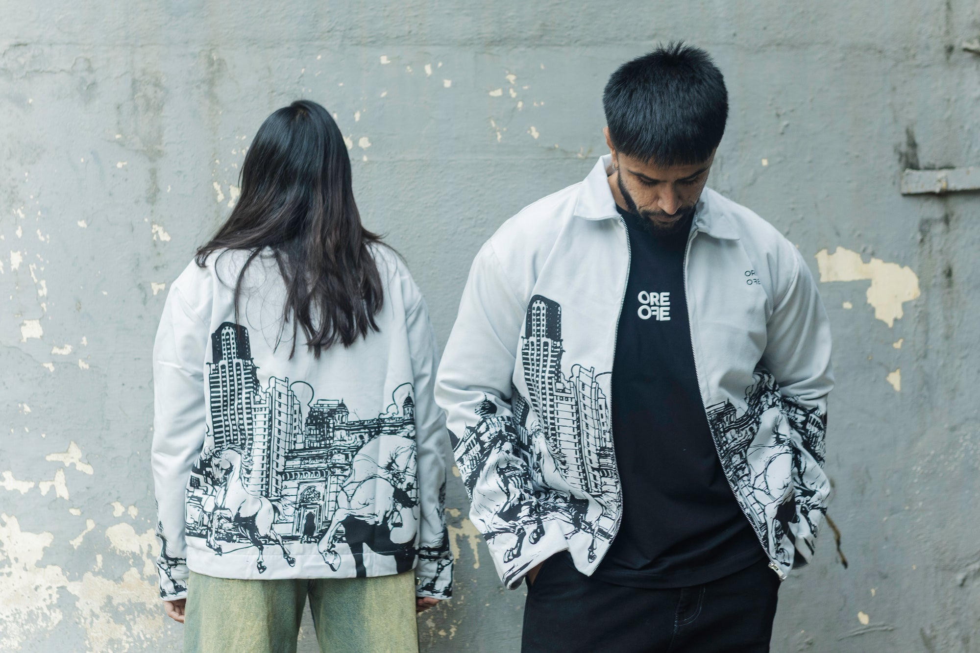 Two people wearing ORE OFE's khwaab jacket & standing in front of a distorted grey wall