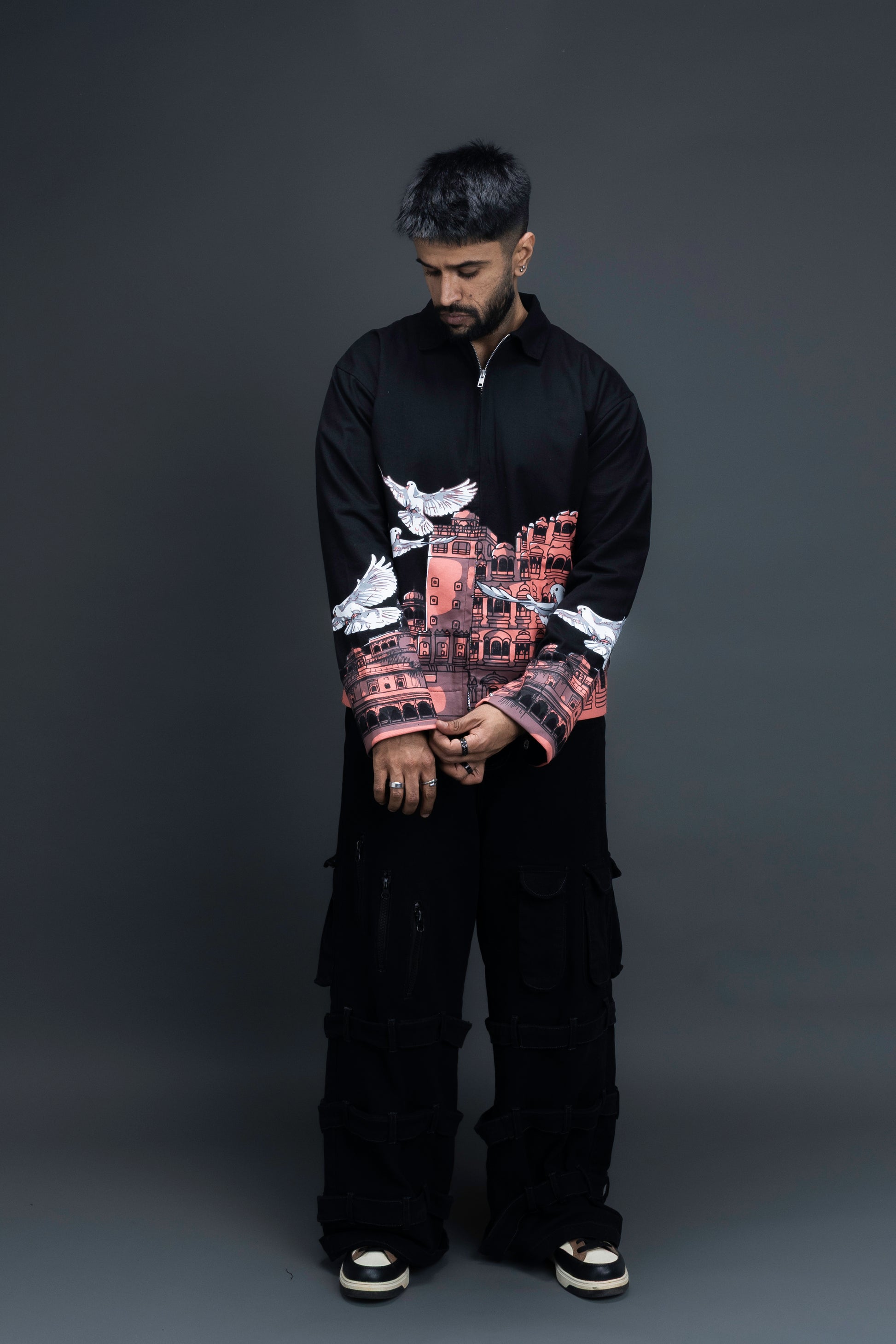 Man wearing ORE OFE's heritage black jacket that is designed on the theme of Hawa mahal standing against a grey background