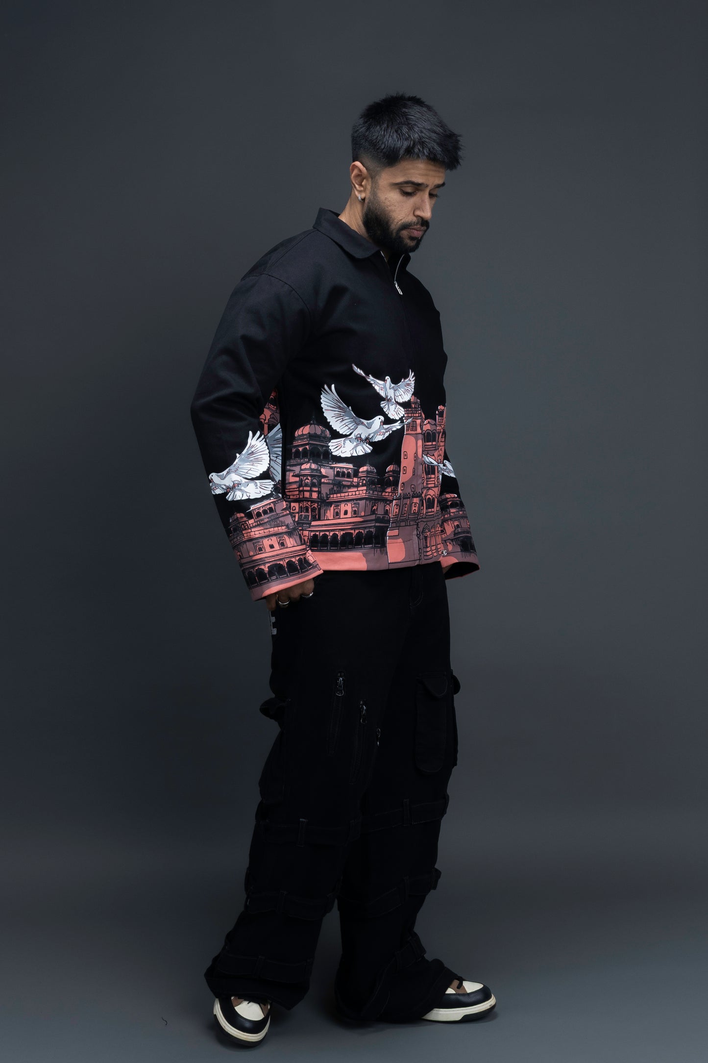 Man wearing ORE OFE's heritage black jacket that is designed on the theme of Hawa mahal standing against a grey background