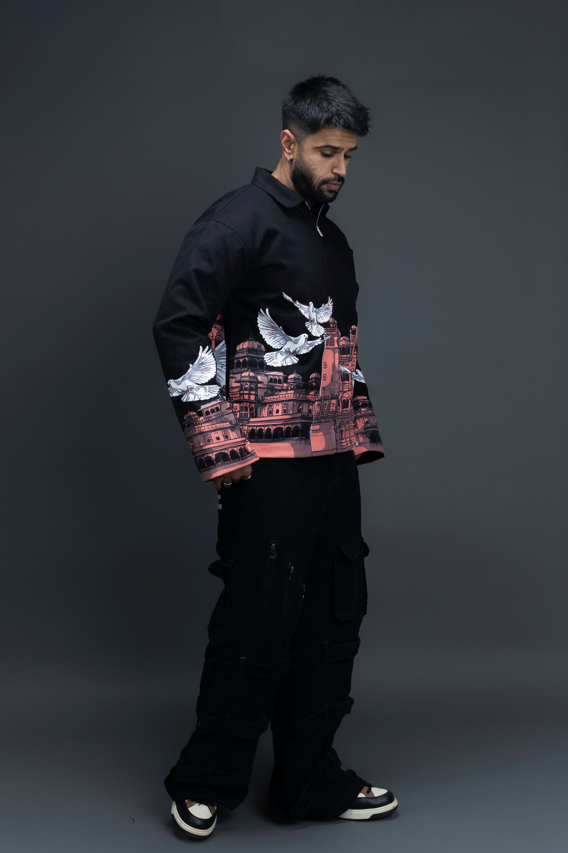 Man wearing ORE OFE's heritage black jacket that is designed on the theme of Hawa mahal standing against a grey background
