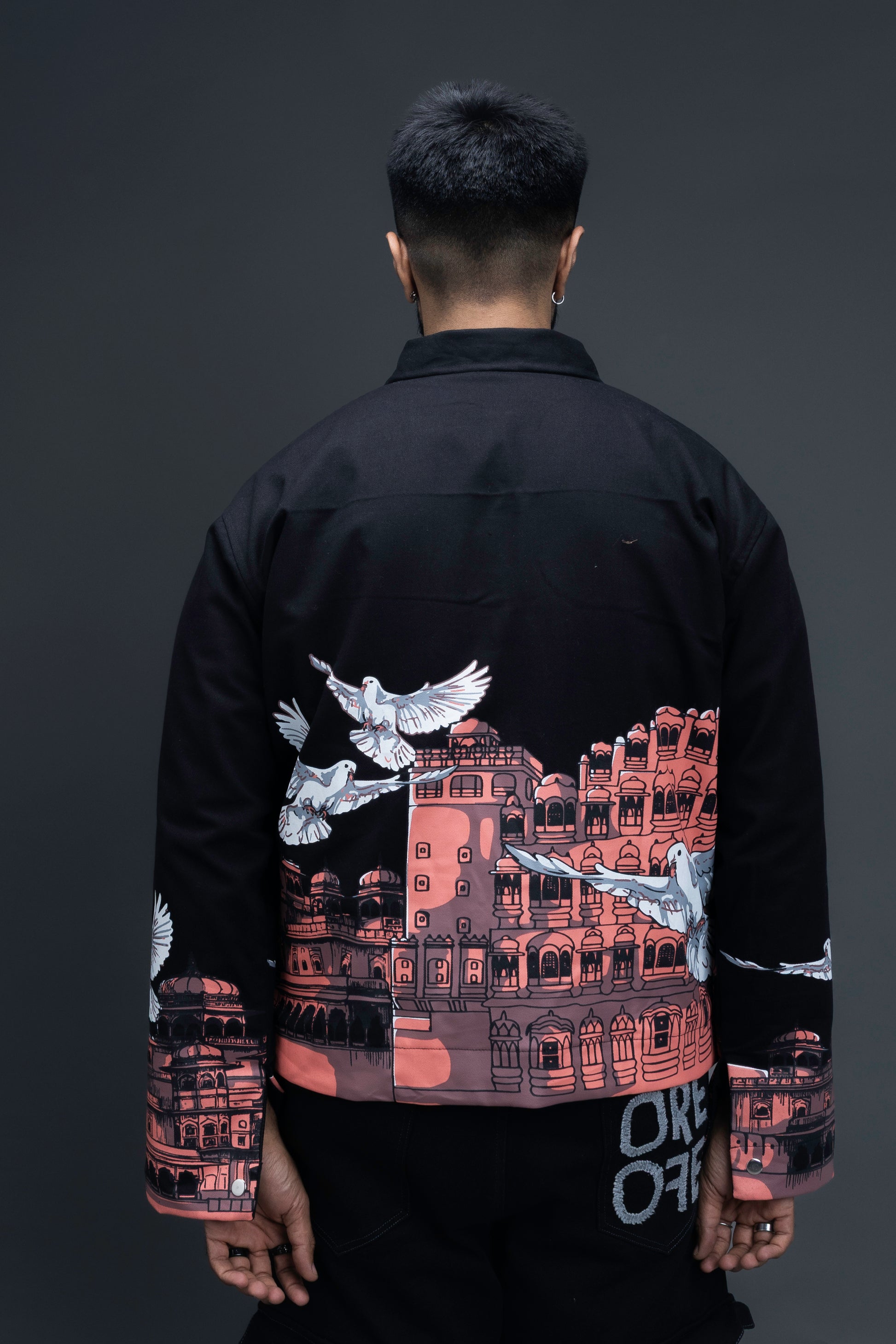Man wearing ORE OFE's heritage black jacket that is designed on the theme of Hawa mahal standing against a grey background