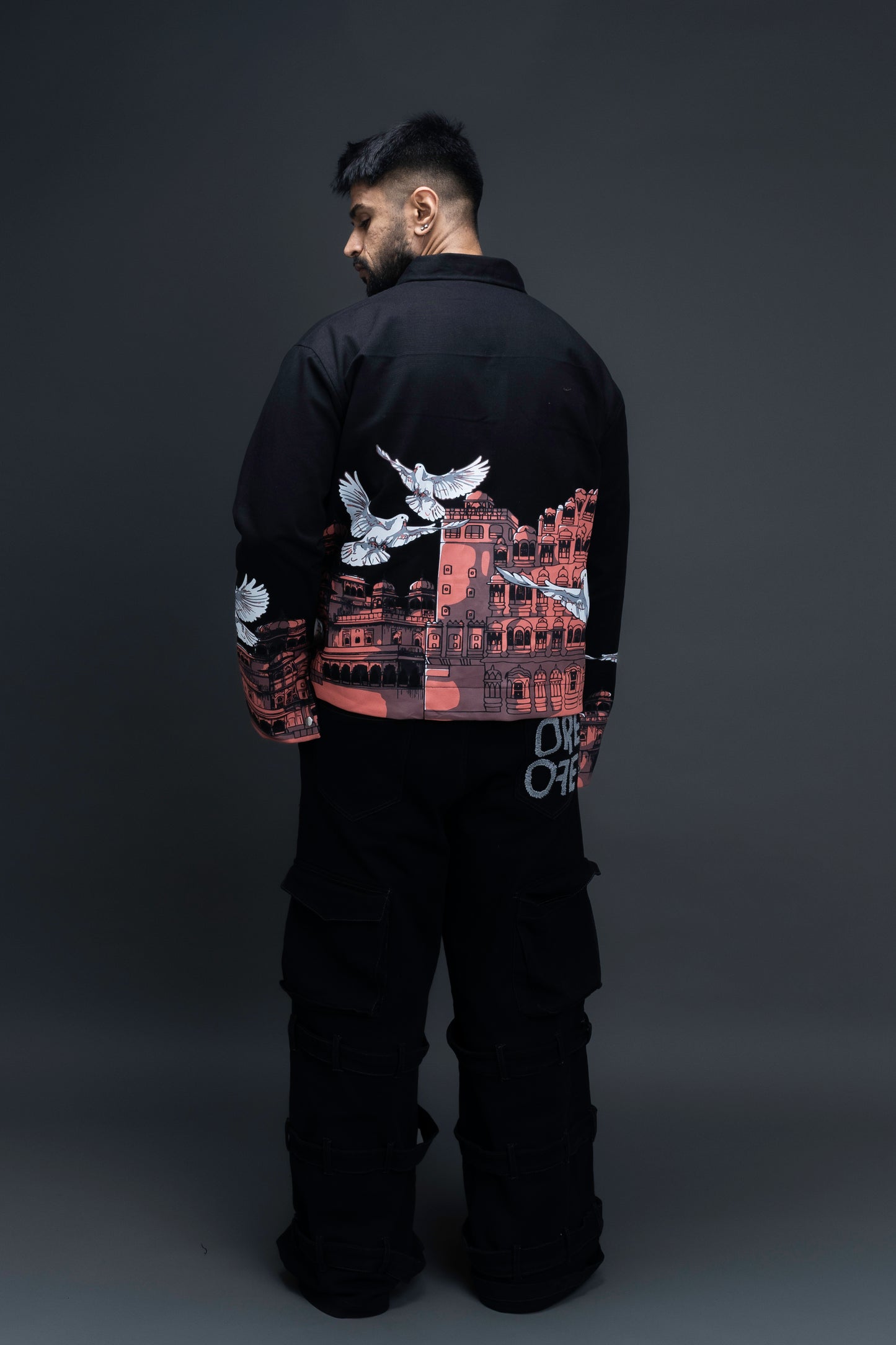 Man wearing ORE OFE's heritage black jacket that is designed on the theme of Hawa mahal standing against a grey background