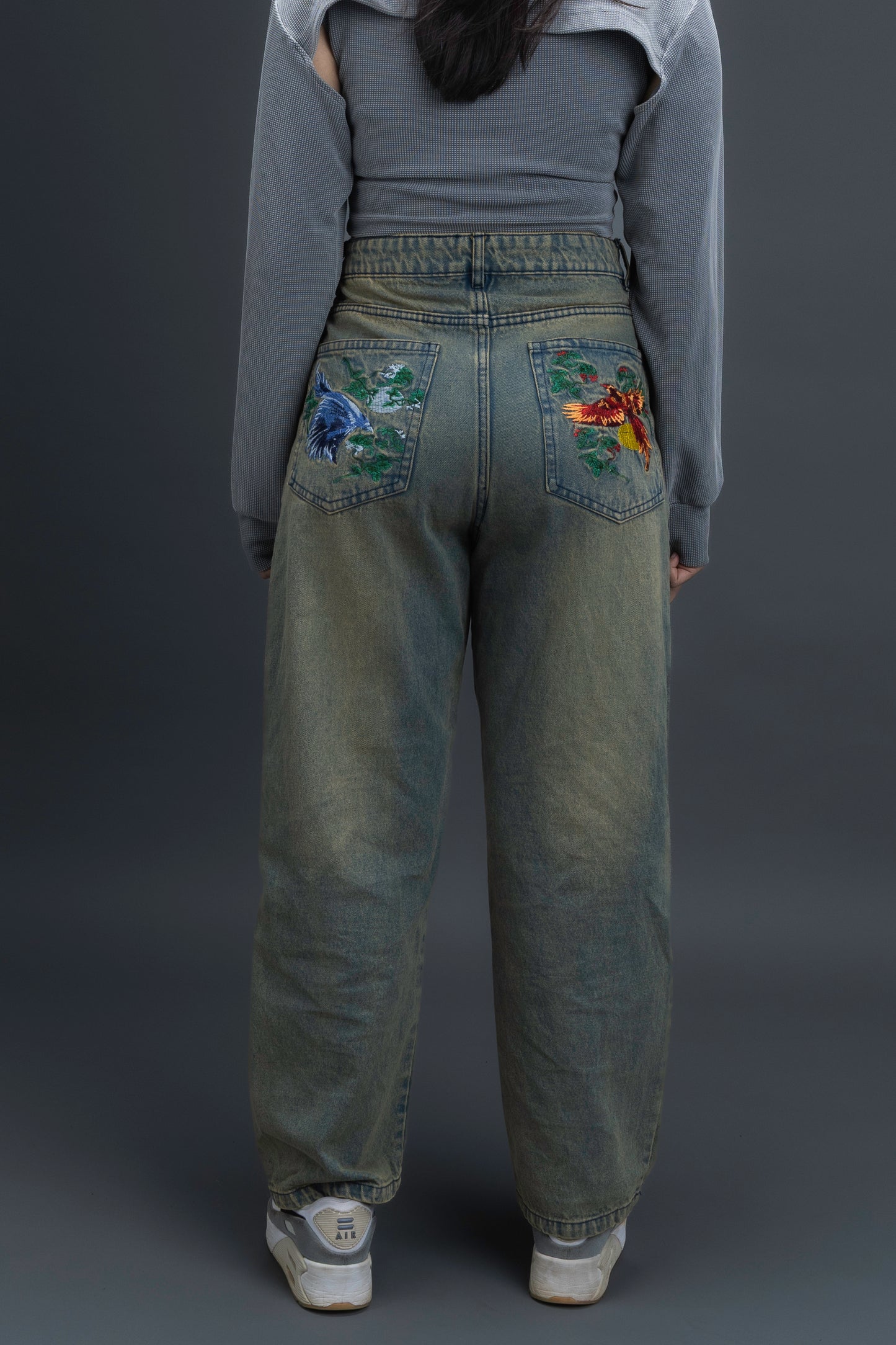 Person wearing ORE OFE's Vintage washed denim that has a pheonix embroided on the back pocket standing against a grey background