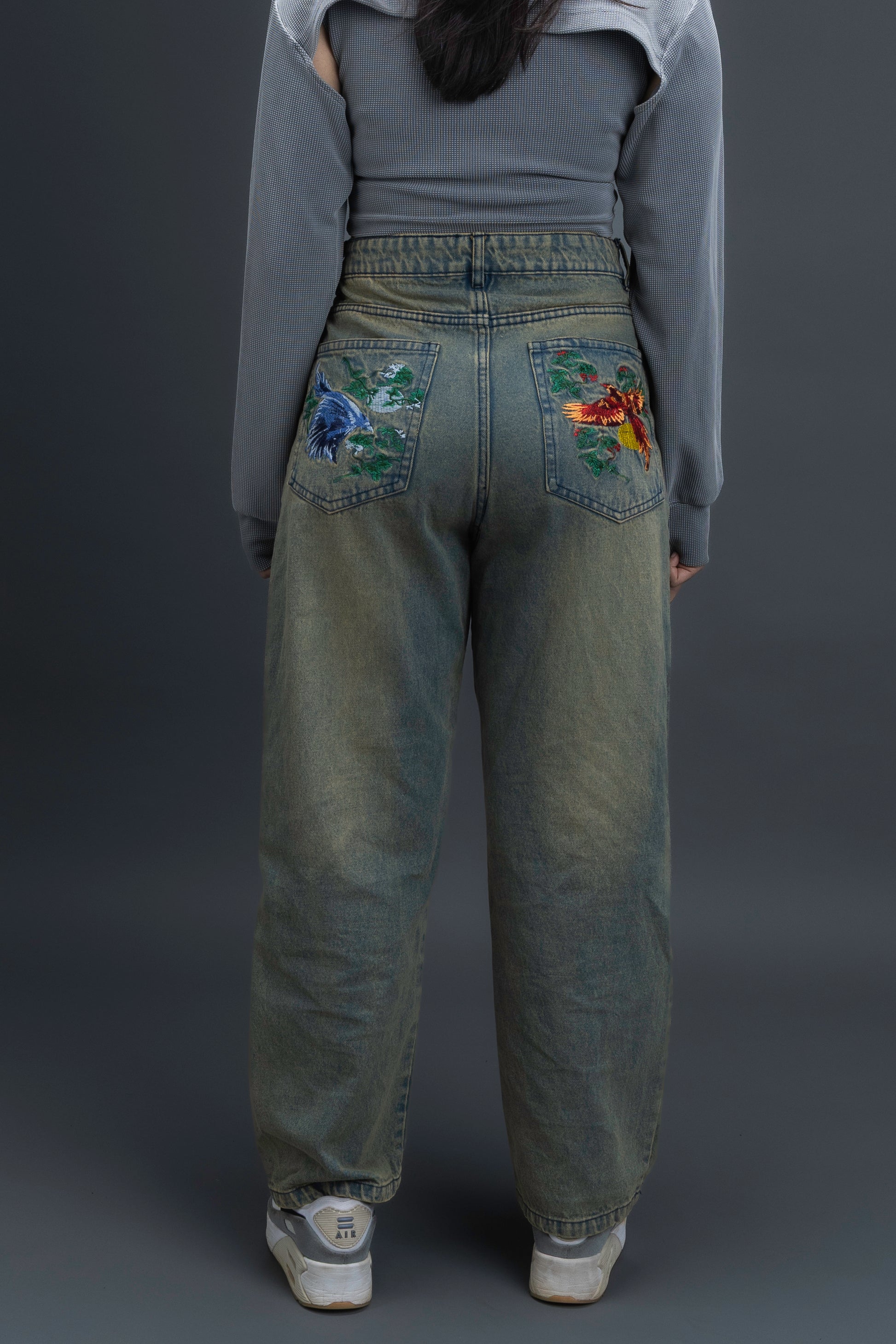Person wearing ORE OFE's Vintage washed denim that has a pheonix embroided on the back pocket standing against a grey background