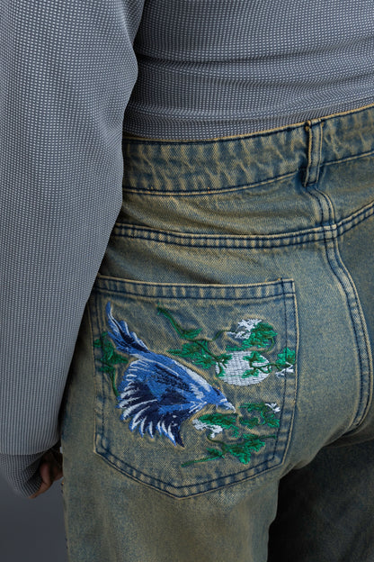 Person wearing ORE OFE's Vintage washed denim that has a pheonix embroided on the back pocket standing against a grey background