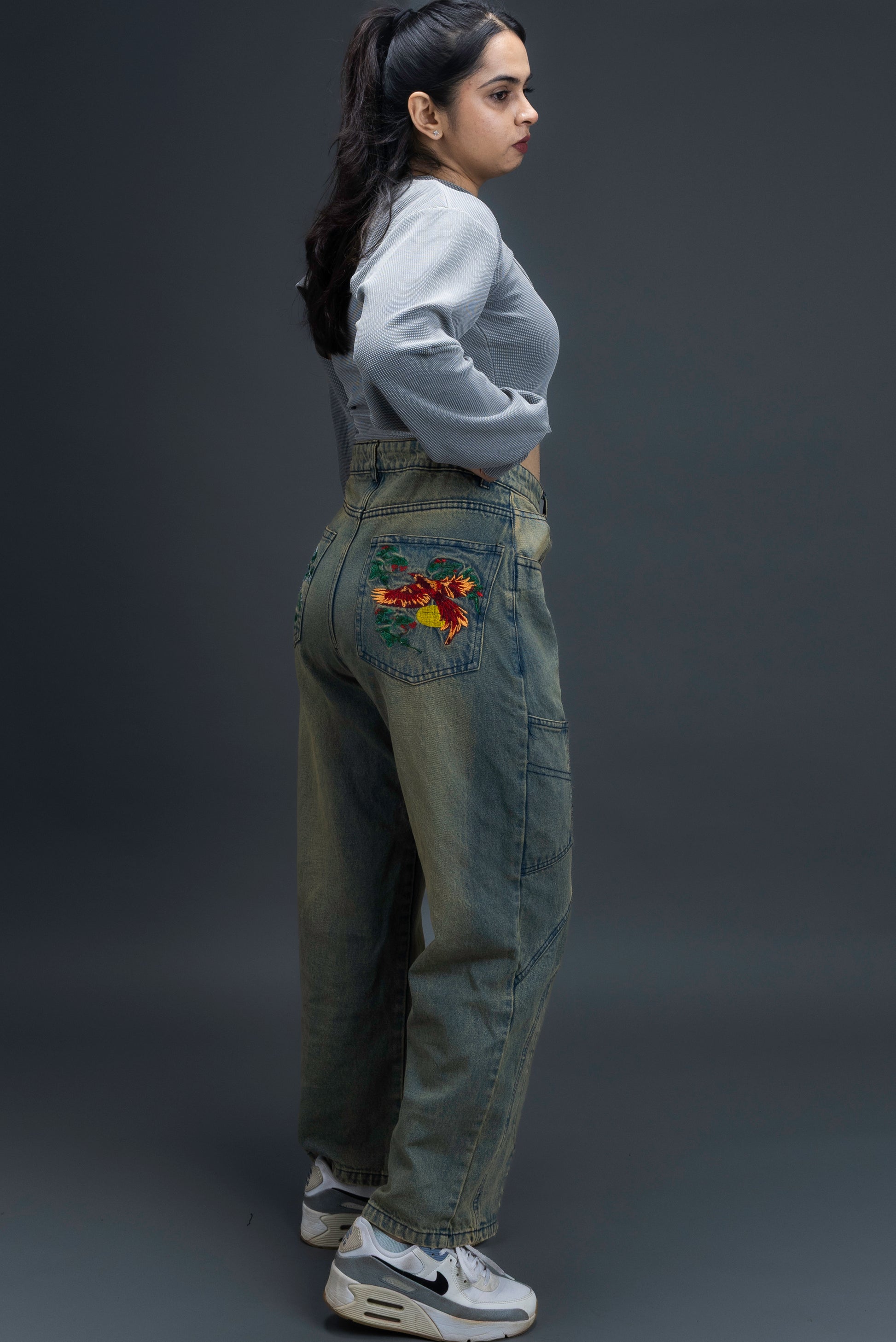 Person wearing ORE OFE's Vintage washed denim that has a pheonix embroided on the back pocket standing against a grey background