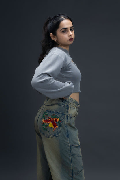 Person wearing ORE OFE's Vintage washed denim that has a pheonix embroided on the back pocket standing against a grey background