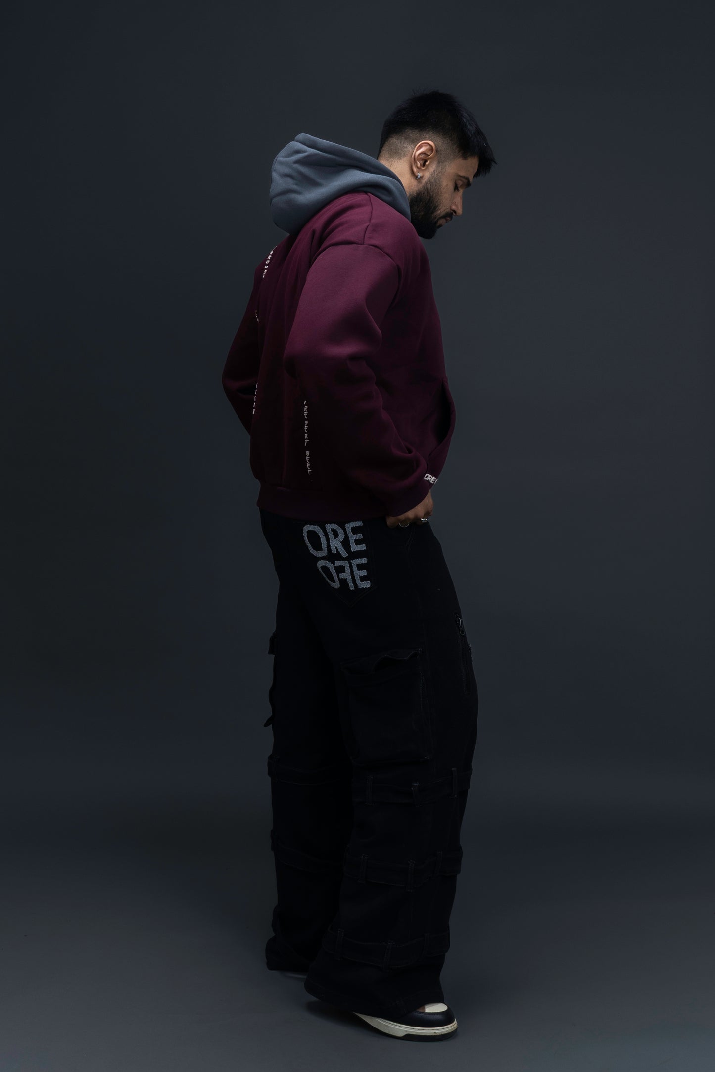 Person wearing a maroon contrast hoodie by ORE OFE with chest & back puff printed design  standaing against  a dark grey background