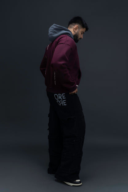 Person wearing a maroon contrast hoodie by ORE OFE with chest & back puff printed design  standaing against  a dark grey background