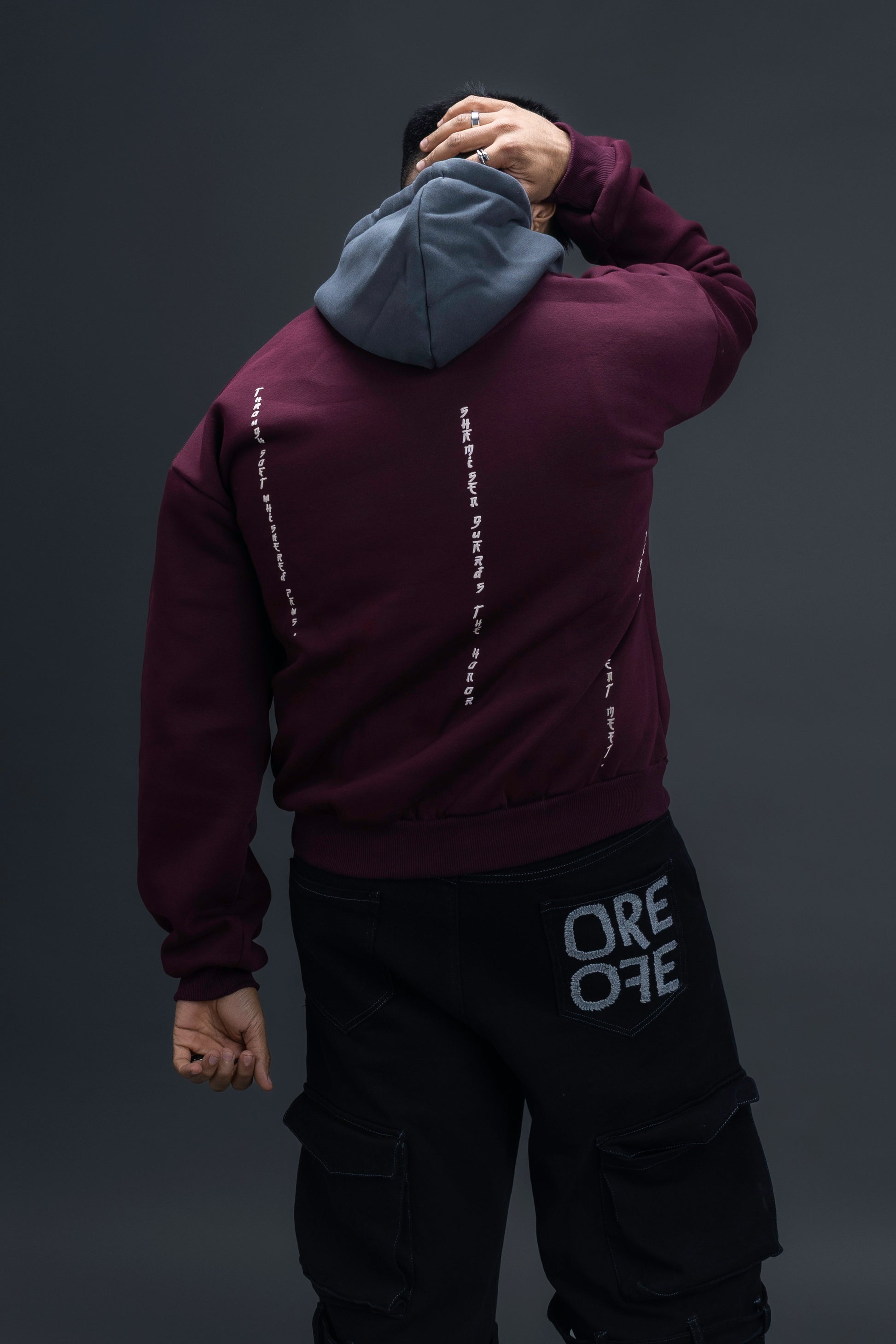 Person wearing a maroon contrast hoodie by ORE OFE with chest & back puff printed design  standaing against  a dark grey background