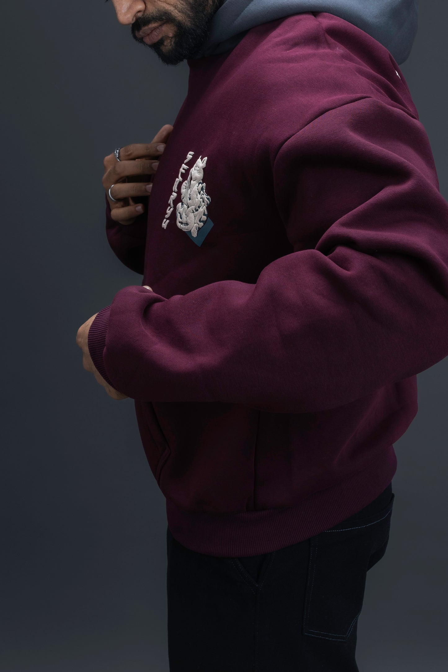 Person wearing a maroon contrast hoodie by ORE OFE with chest & back puff printed design  standaing against  a dark grey background