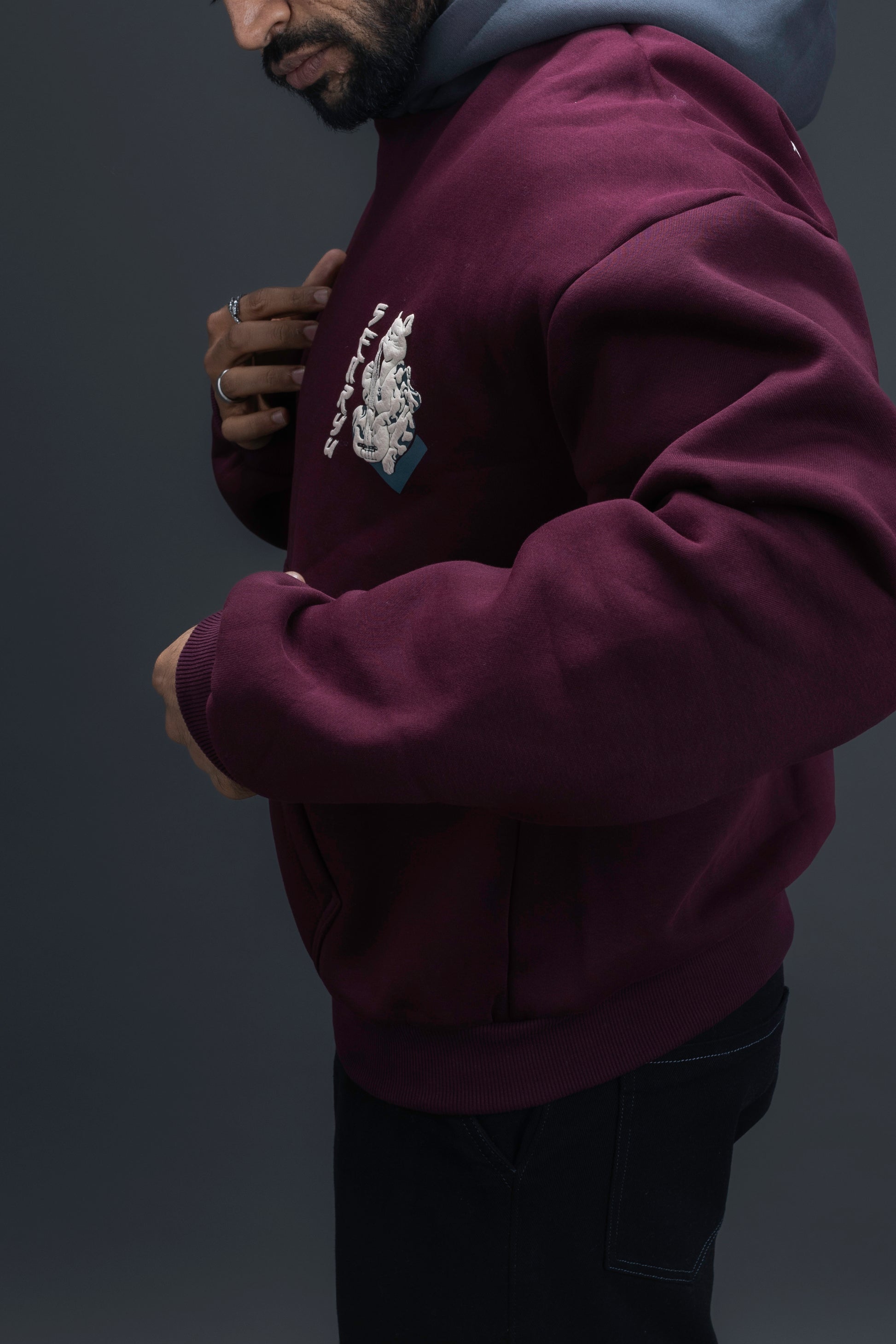 Person wearing a maroon contrast hoodie by ORE OFE with chest & back puff printed design  standaing against  a dark grey background