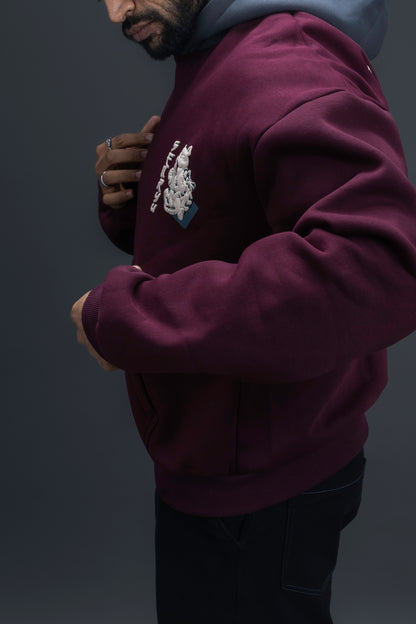 Person wearing a maroon contrast hoodie by ORE OFE with chest & back puff printed design  standaing against  a dark grey background
