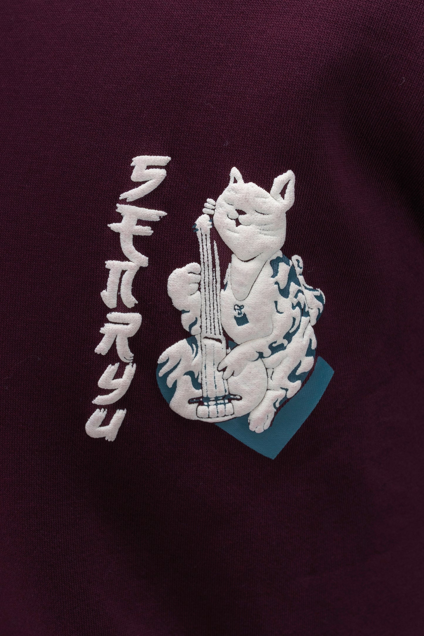 Person wearing a maroon contrast hoodie by ORE OFE with chest & back puff printed design  standaing against  a dark grey background