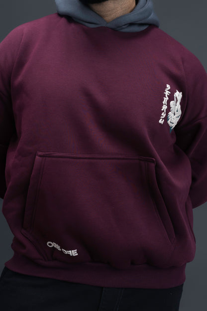 Person wearing a maroon contrast hoodie by ORE OFE with chest & back puff printed design  standaing against  a dark grey background