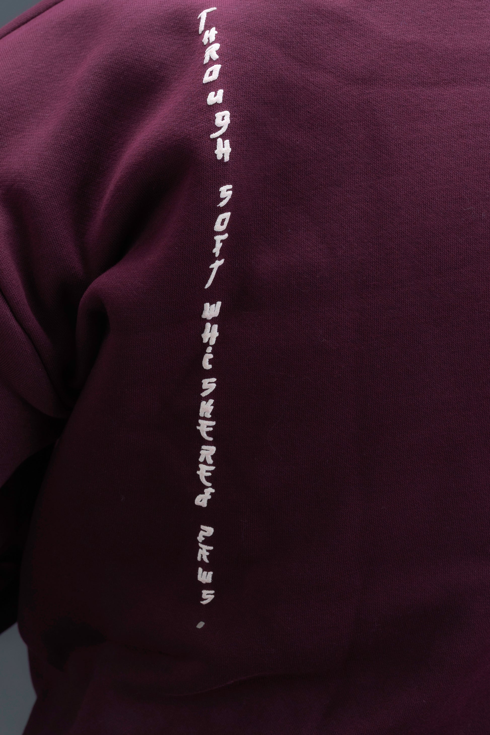 Person wearing a maroon contrast hoodie by ORE OFE with chest & back puff printed design  standaing against  a dark grey background