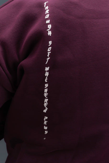 Person wearing a maroon contrast hoodie by ORE OFE with chest & back puff printed design  standaing against  a dark grey background
