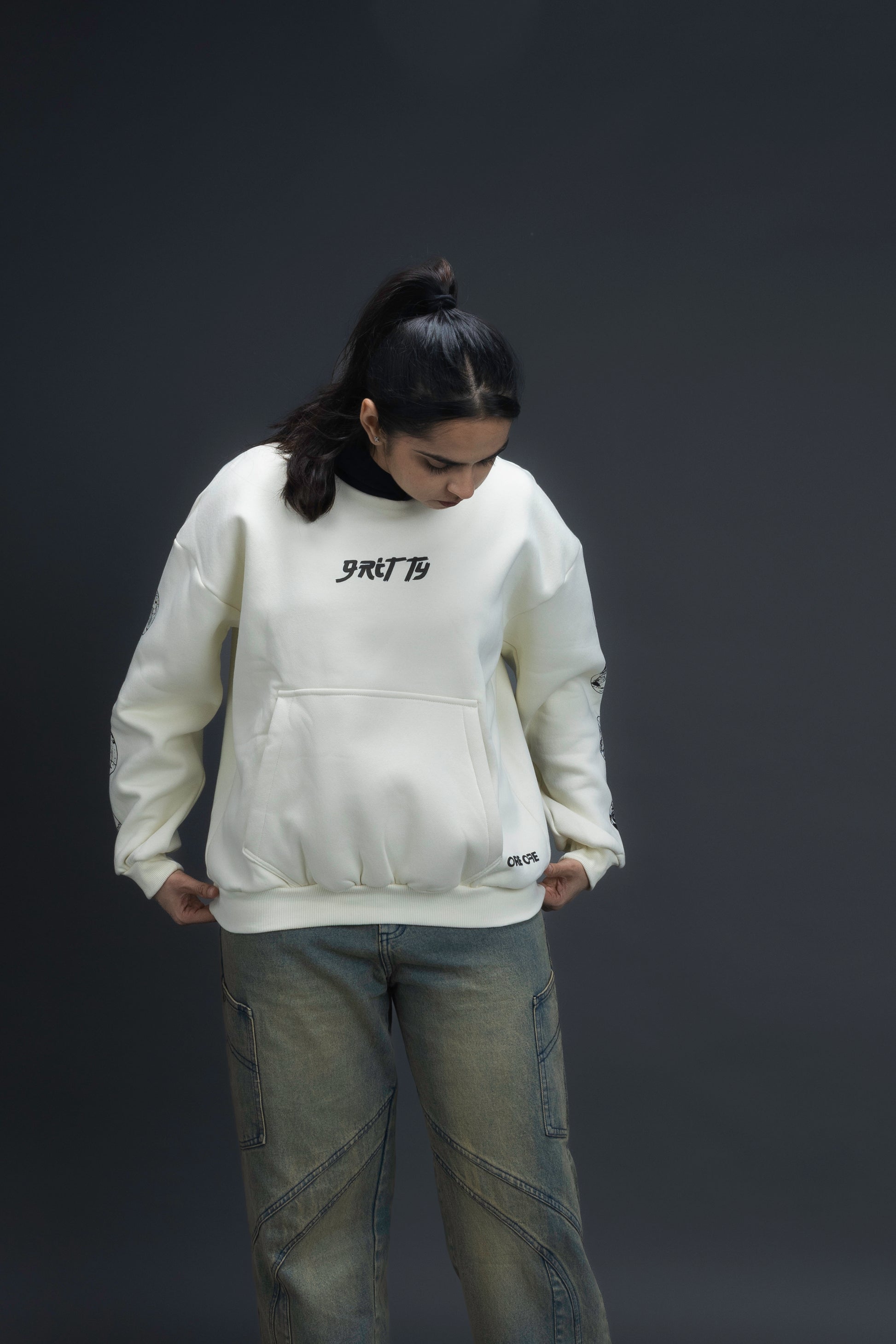 Person wearing a off-white contrast hoodie by ORE OFE with text on the chest that reads GRITTY & design on both sleeves, standing against a black background 