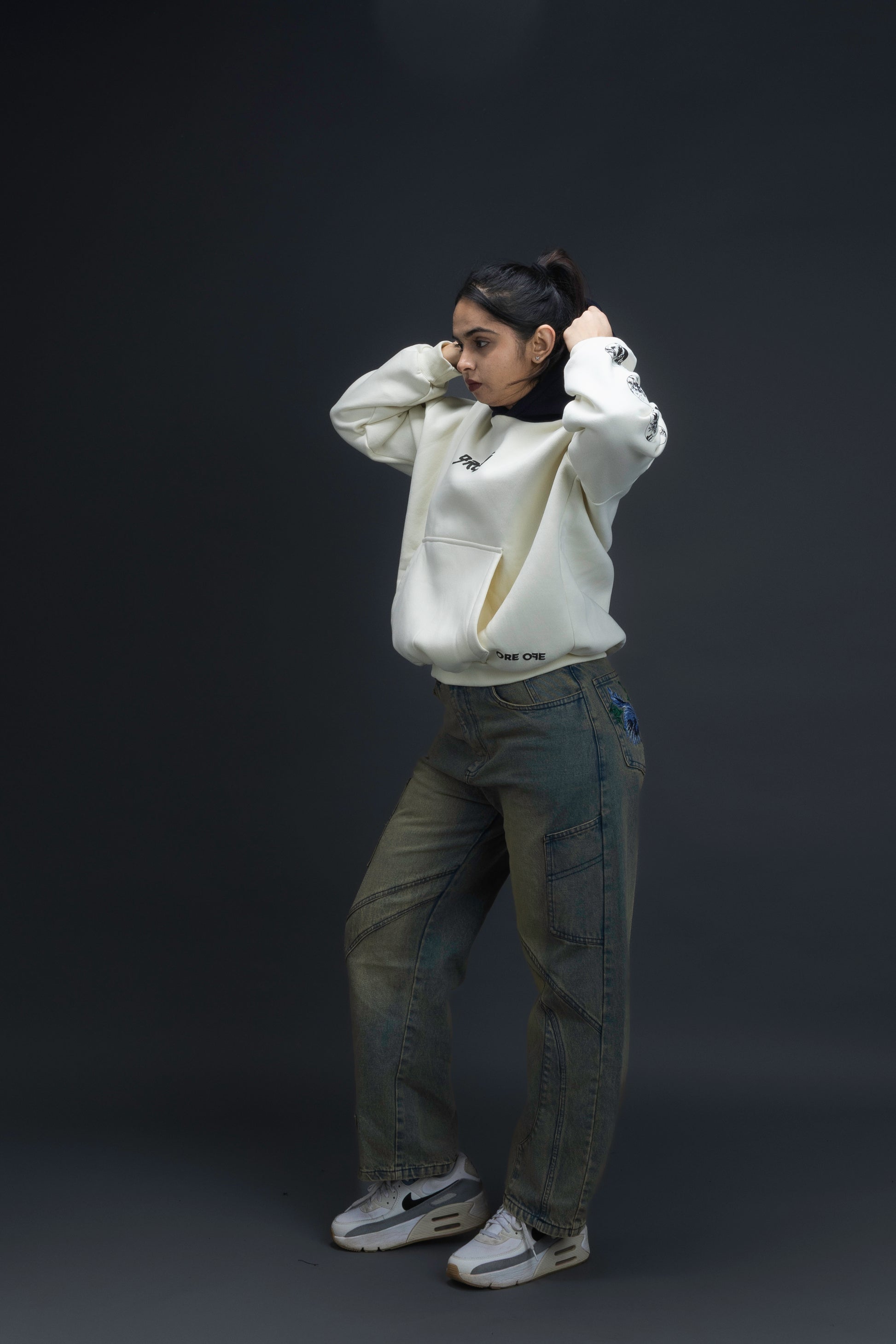 Person wearing a off-white contrast hoodie by ORE OFE with text on the chest that reads GRITTY & design on both sleeves, standing against a black background 