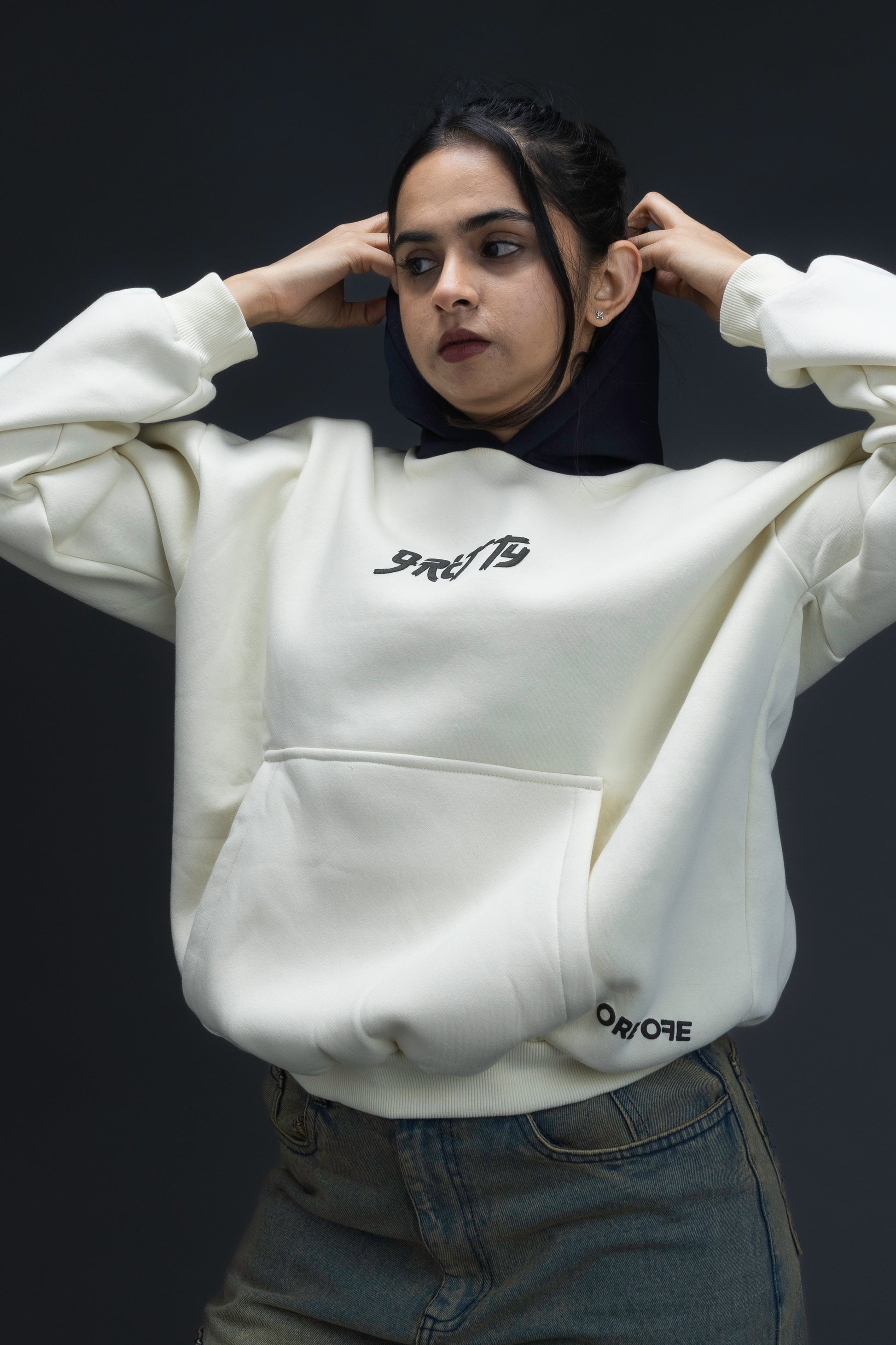Person wearing a off-white contrast hoodie by ORE OFE with text on the chest that reads GRITTY, standing against a black background