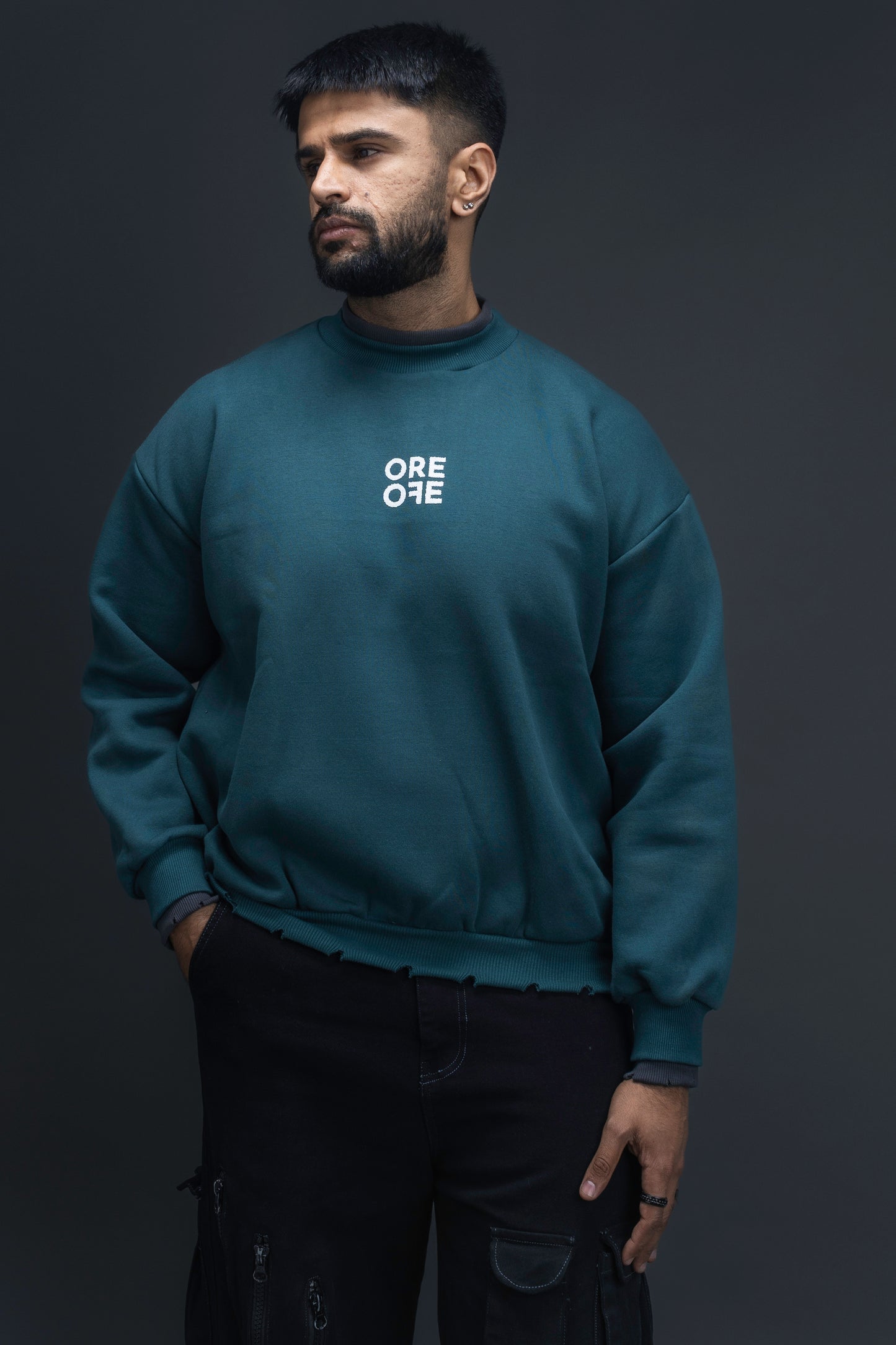 Man wearing ORE OFEs green contrast sweatshirt with the logo on the centre of the chest standing against a grey background
