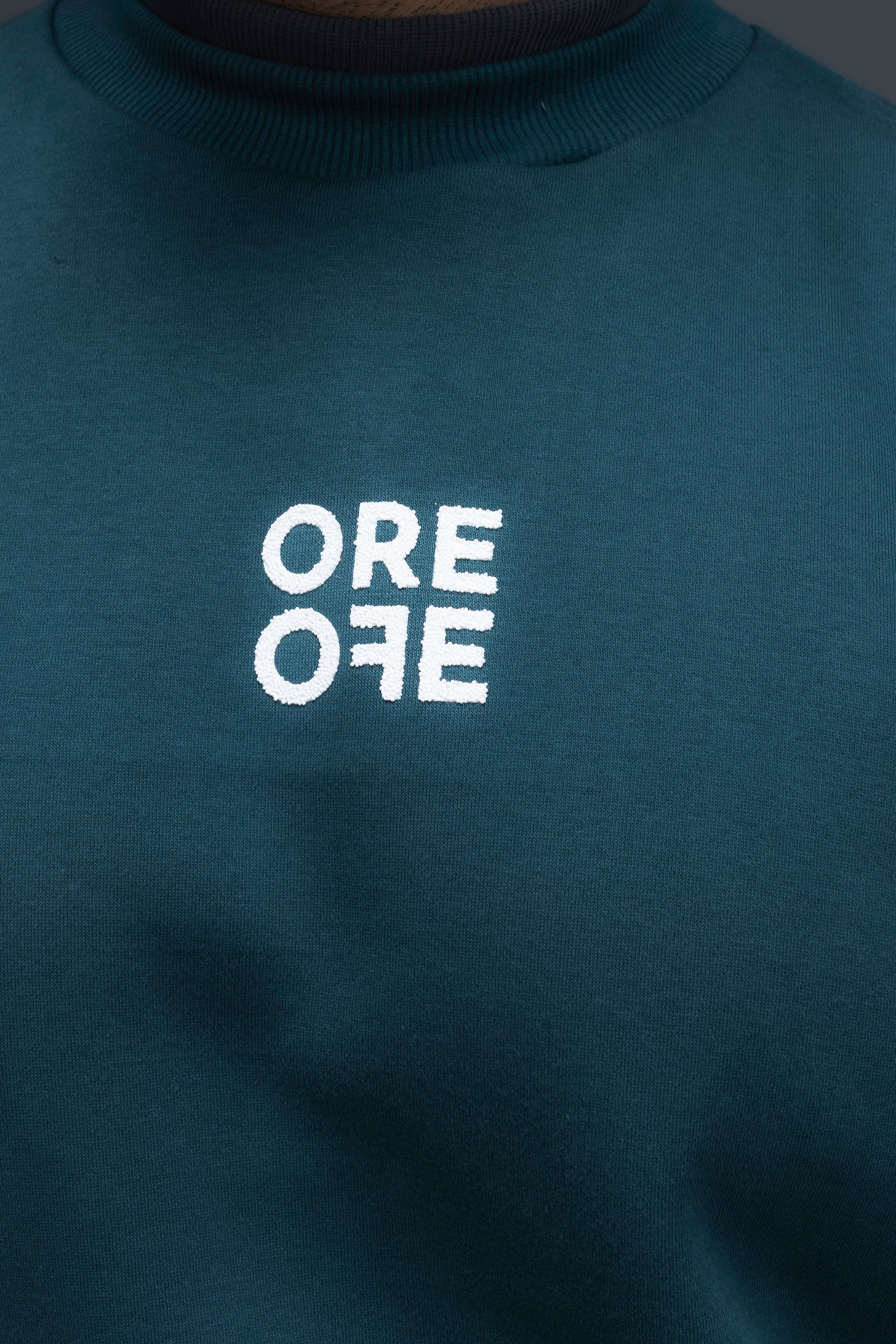 Man wearing ORE OFEs green contrast sweatshirt with the logo on the centre of the chest standing against a grey background