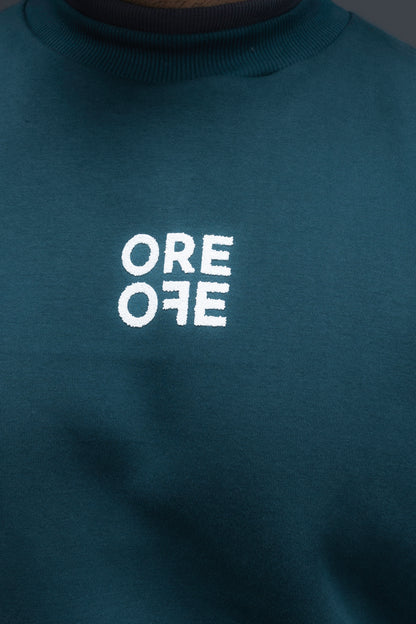 Man wearing ORE OFEs green contrast sweatshirt with the logo on the centre of the chest standing against a grey background