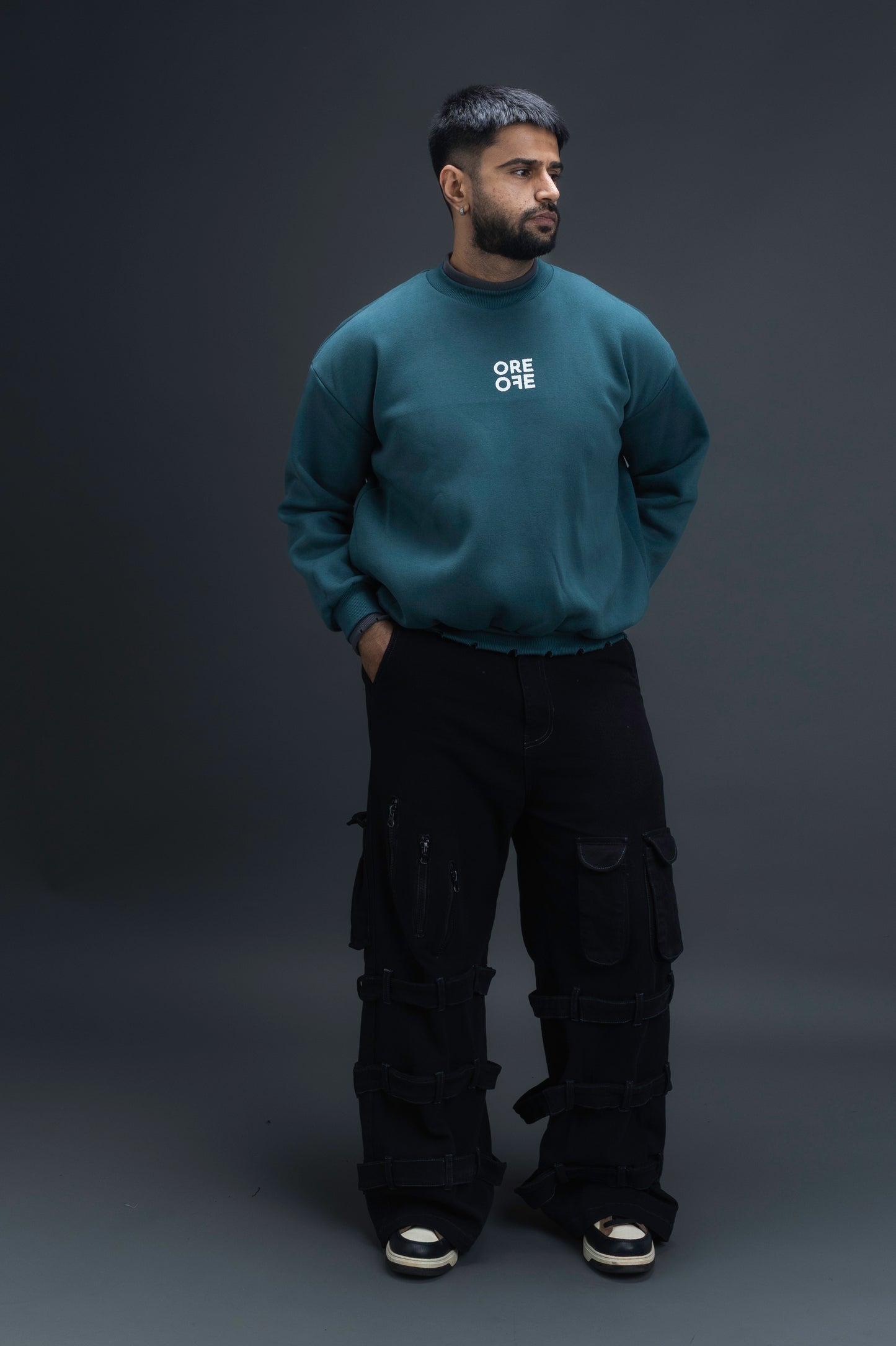 Man wearing ORE OFEs green contrast sweatshirt with the logo on the centre of the chest standing against a grey background