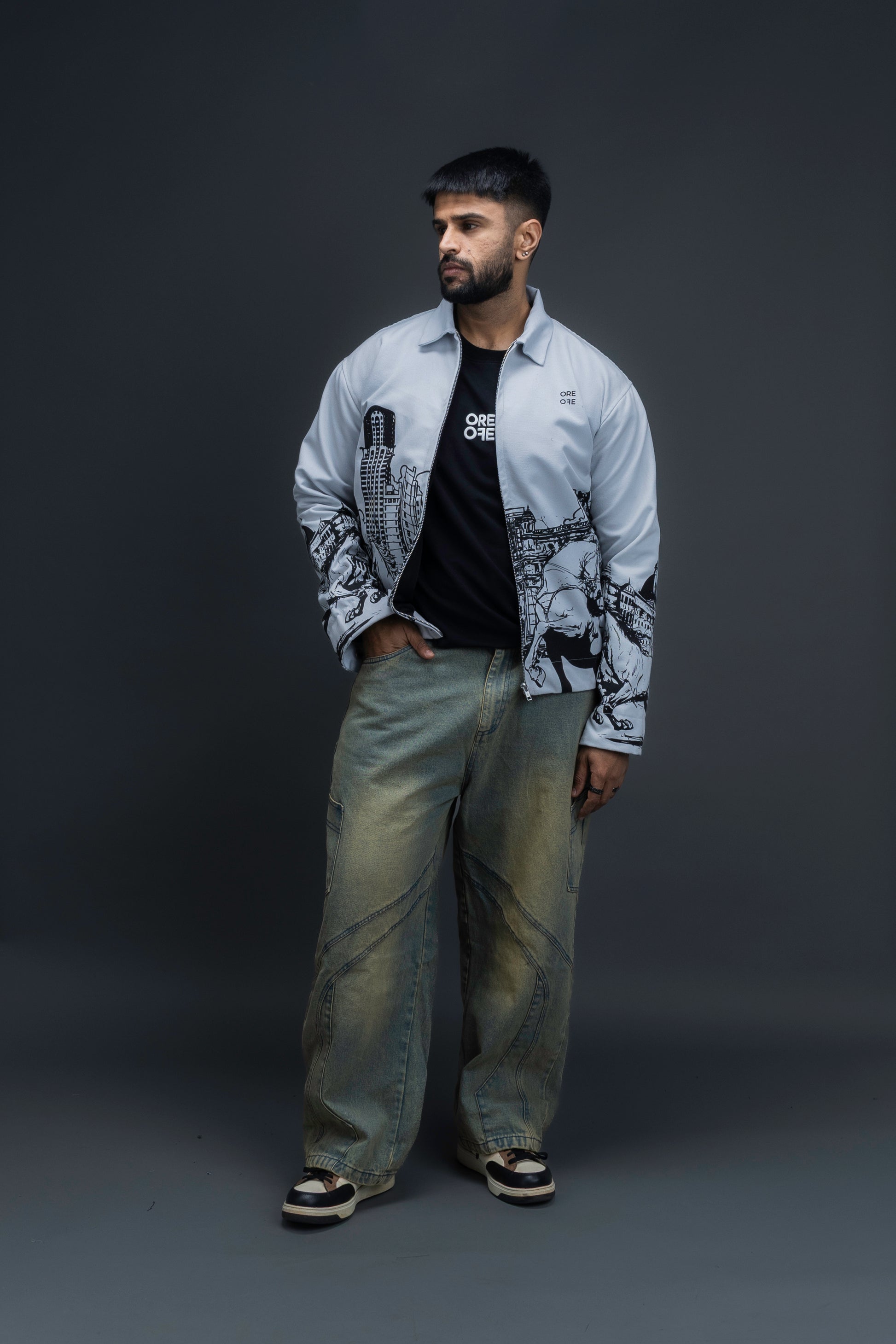 Person wearing ORE OFE's light grey jacket that has the Bombay skyline with horses printed on it standing against a dark grey background