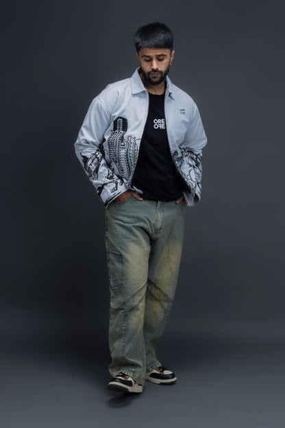 Person wearing ORE OFE's light grey jacket that has the Bombay skyline with horses printed on it standing against a dark grey background