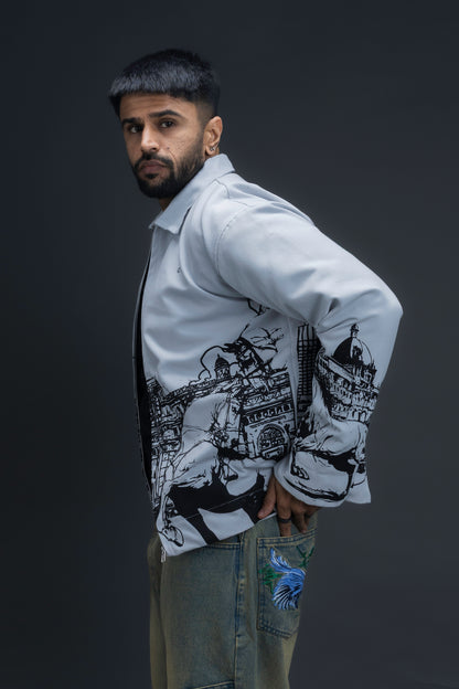 Person wearing ORE OFE's light grey jacket that has the Bombay skyline with horses printed on it standing against a dark grey background