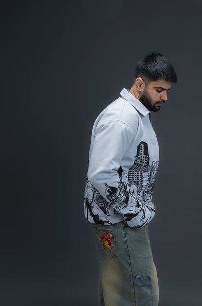 Person wearing ORE OFE's light grey jacket that has the Bombay skyline with horses printed on it standing against a dark grey background