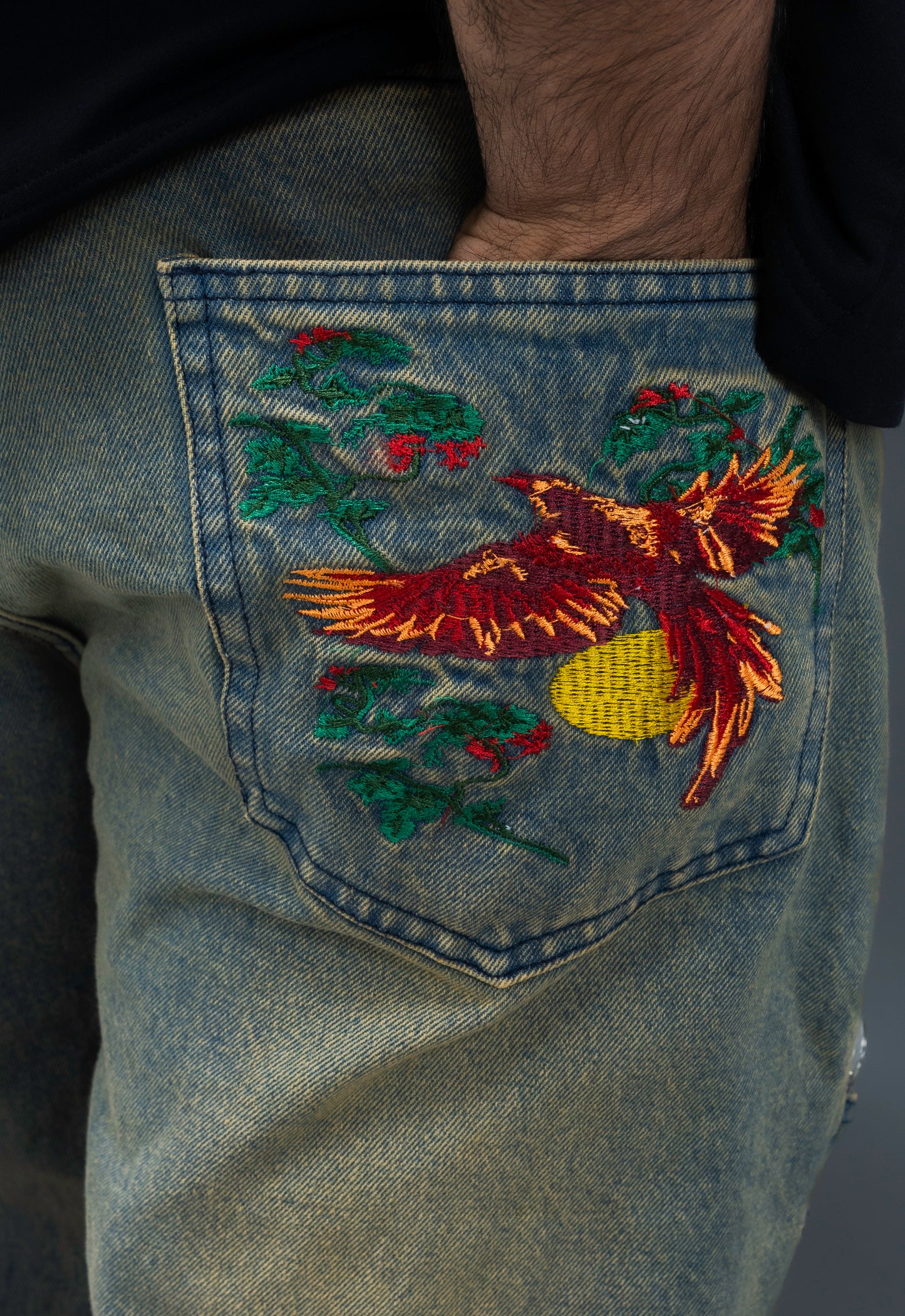 Embroidered design on a denim fabric with a bird and floral elements.
